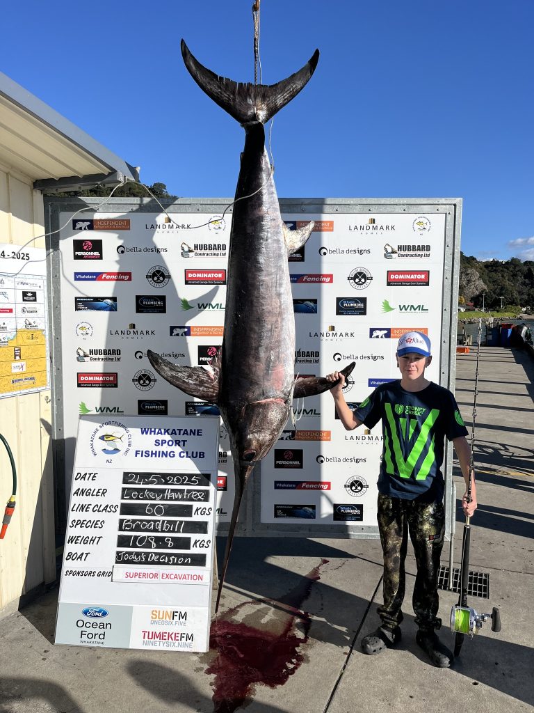 Lockey Hawtree stands beside Whakatane Sport Fishing Club’s weigh board // Photo credit: Waihau Bay Sport Fishing Club