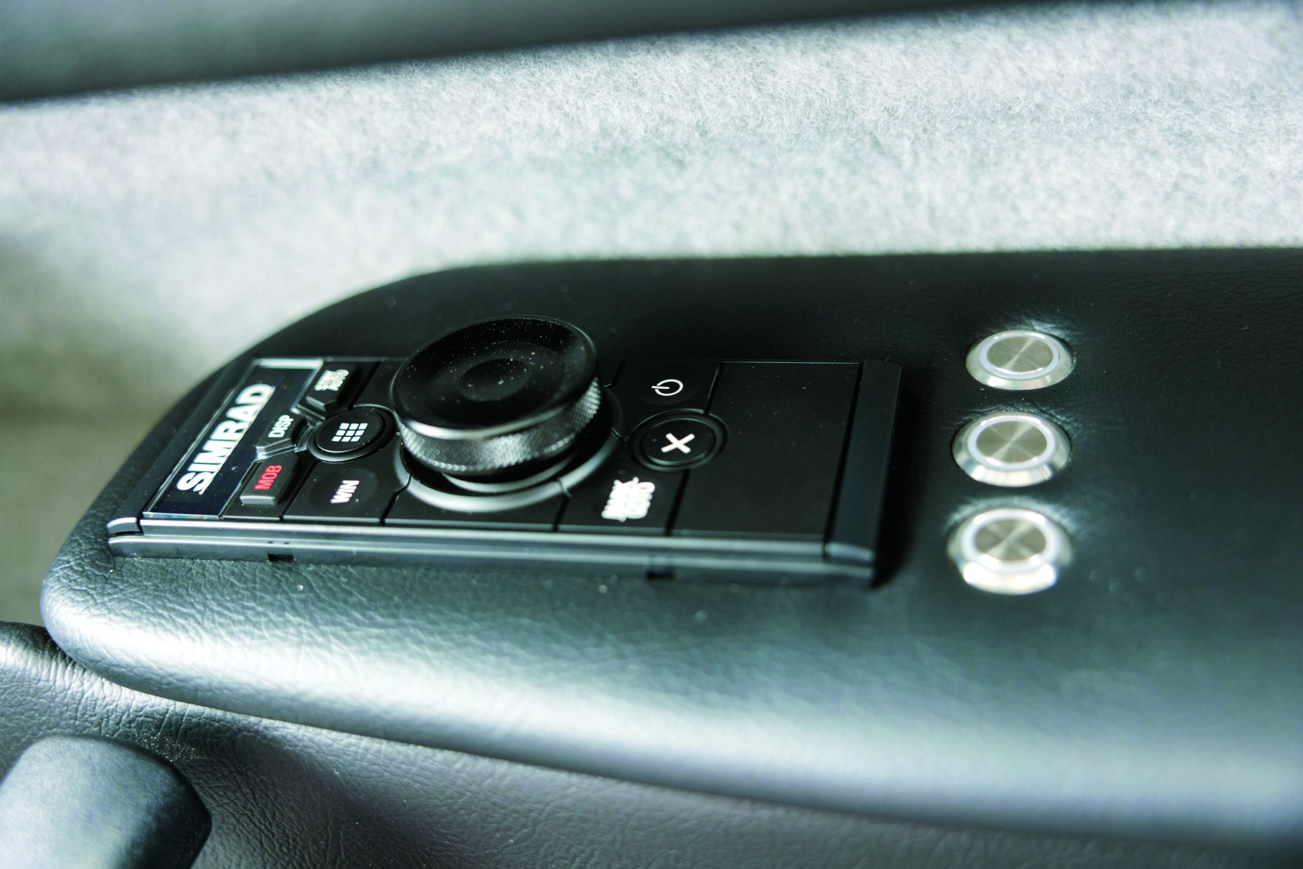 A Simrad marine electronics control panel with navigation dial and buttons is mounted on the dashboard of a boat's helm station // Photo credit: supplied.