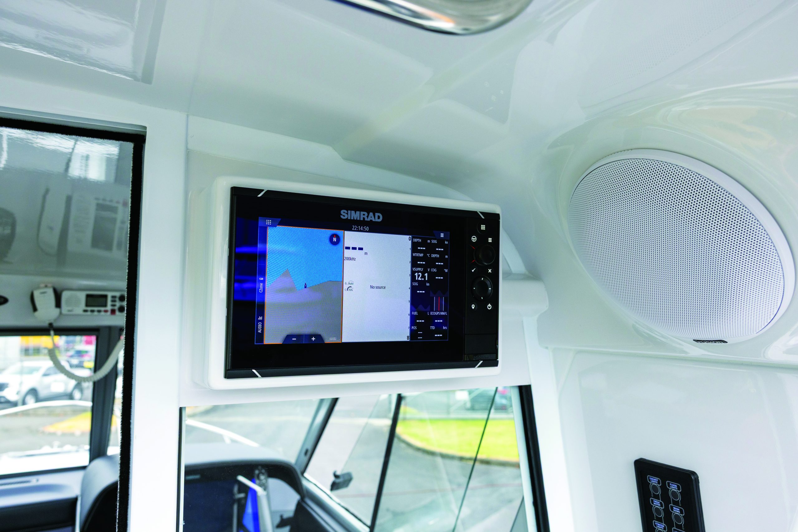 A boat's helm station displays a Simrad navigation system showing chart and radar data while docked at a marina // Photo credit: supplied.