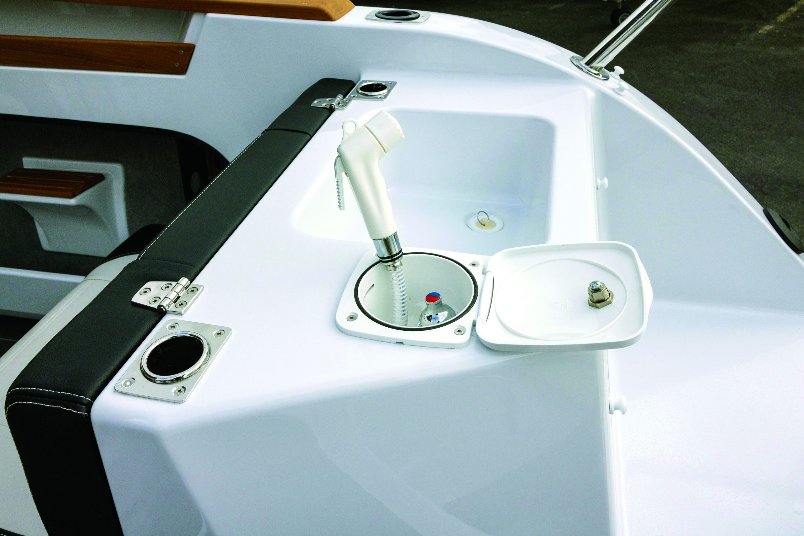A white boat deck features an installed bilge pump with manual handle alongside built-in storage compartments and black safety strapping // Photo credit: supplied.