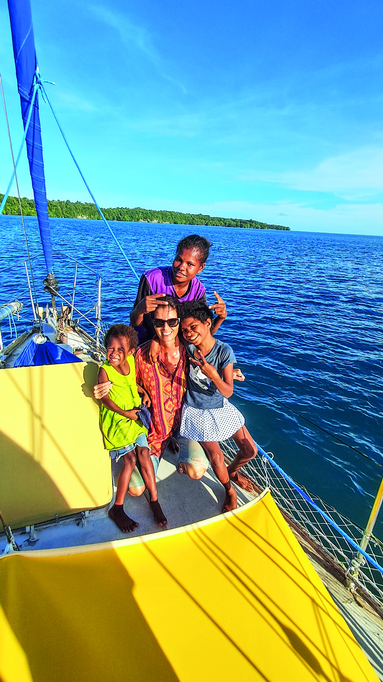 A family enjoys a sunny day sailing on a yellow boat in tropical blue waters with a lush green coastline visible in the background // Photo credit: BIRGIT HAKL.