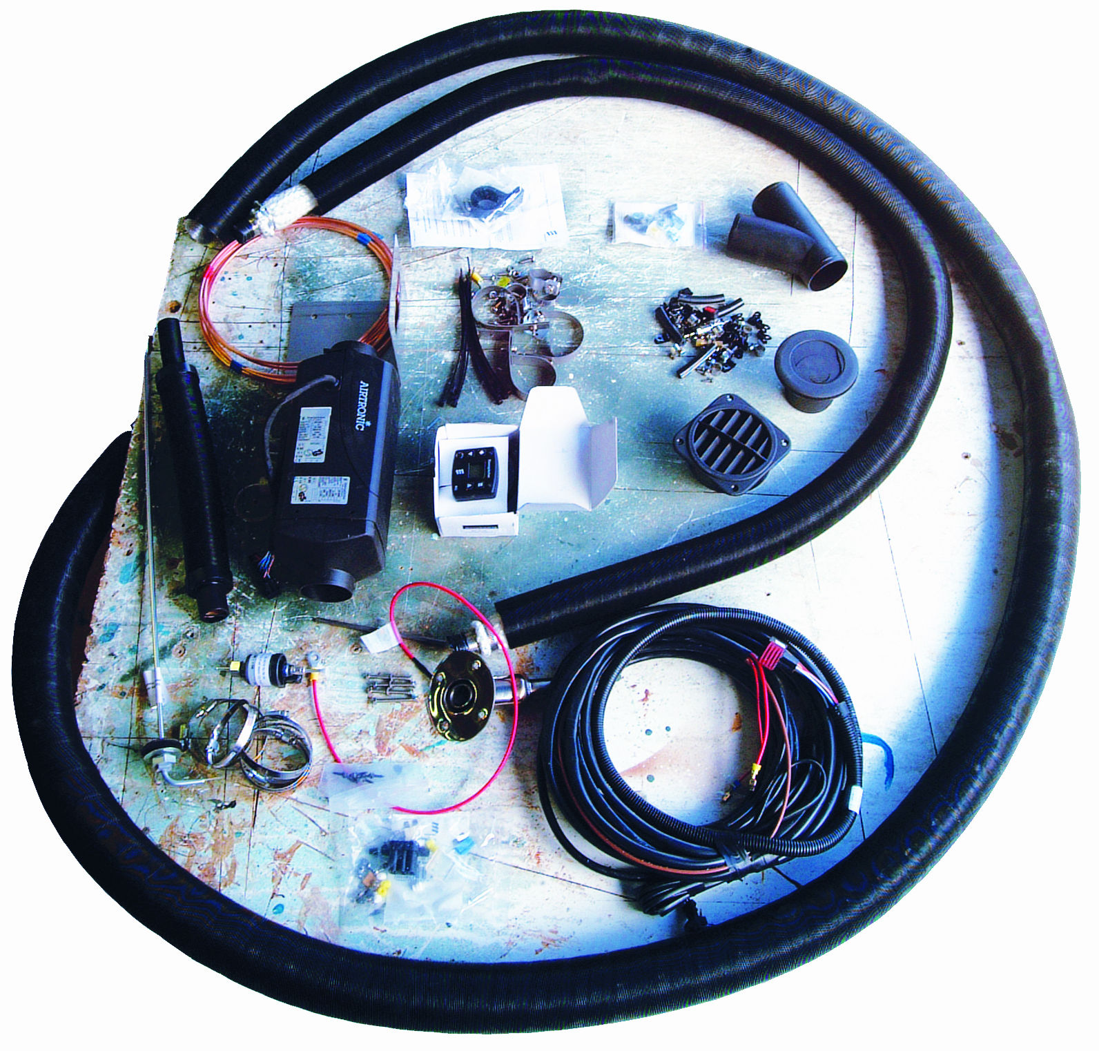 Various marine equipment and parts including hoses, wiring, and mechanical components are laid out in a circular arrangement on a paint-splattered workshop floor // Photo credit: supplied.