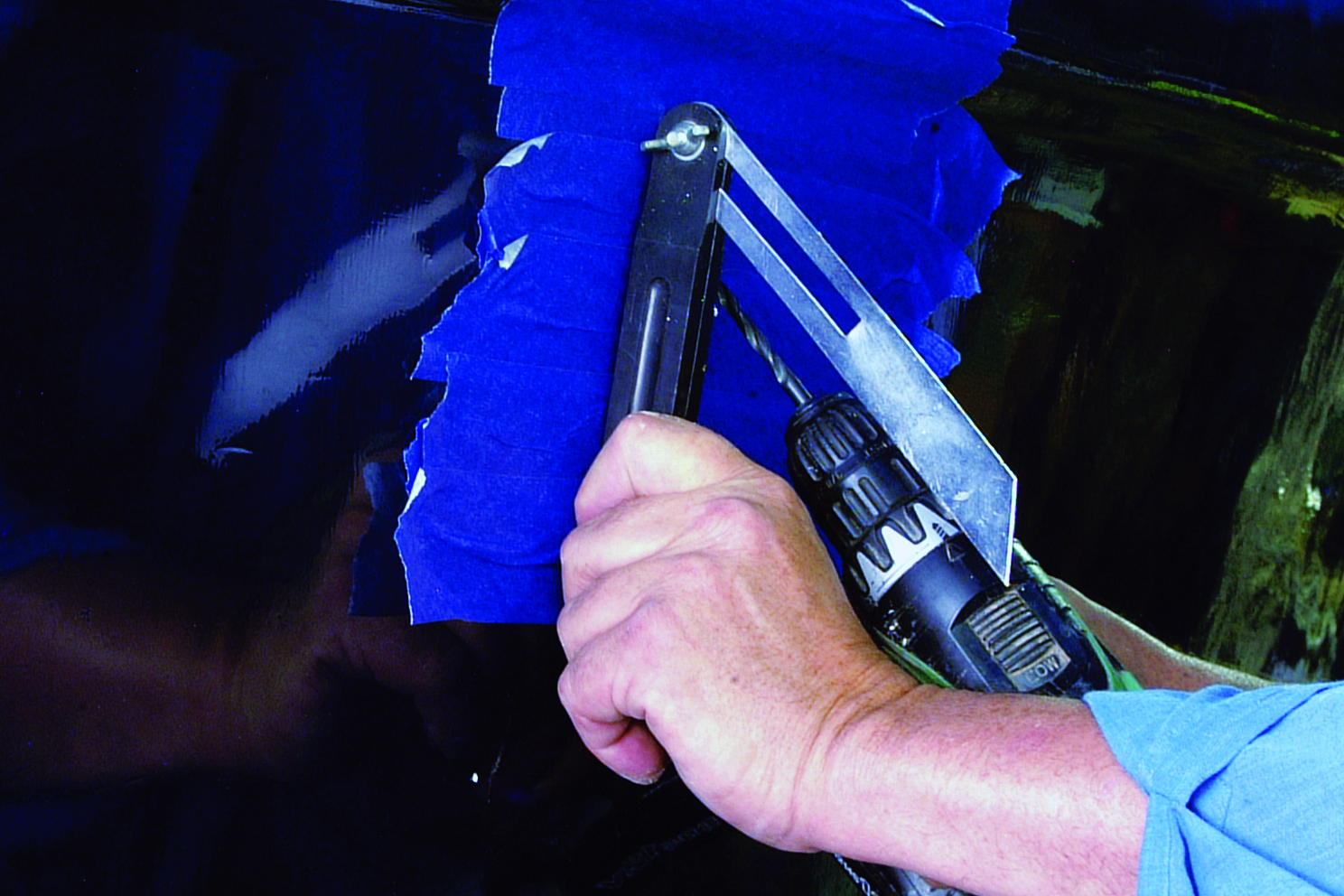 A person uses a handheld tool to scrape blue paint from what appears to be a boat hull during maintenance or restoration work // Photo credit: supplied.