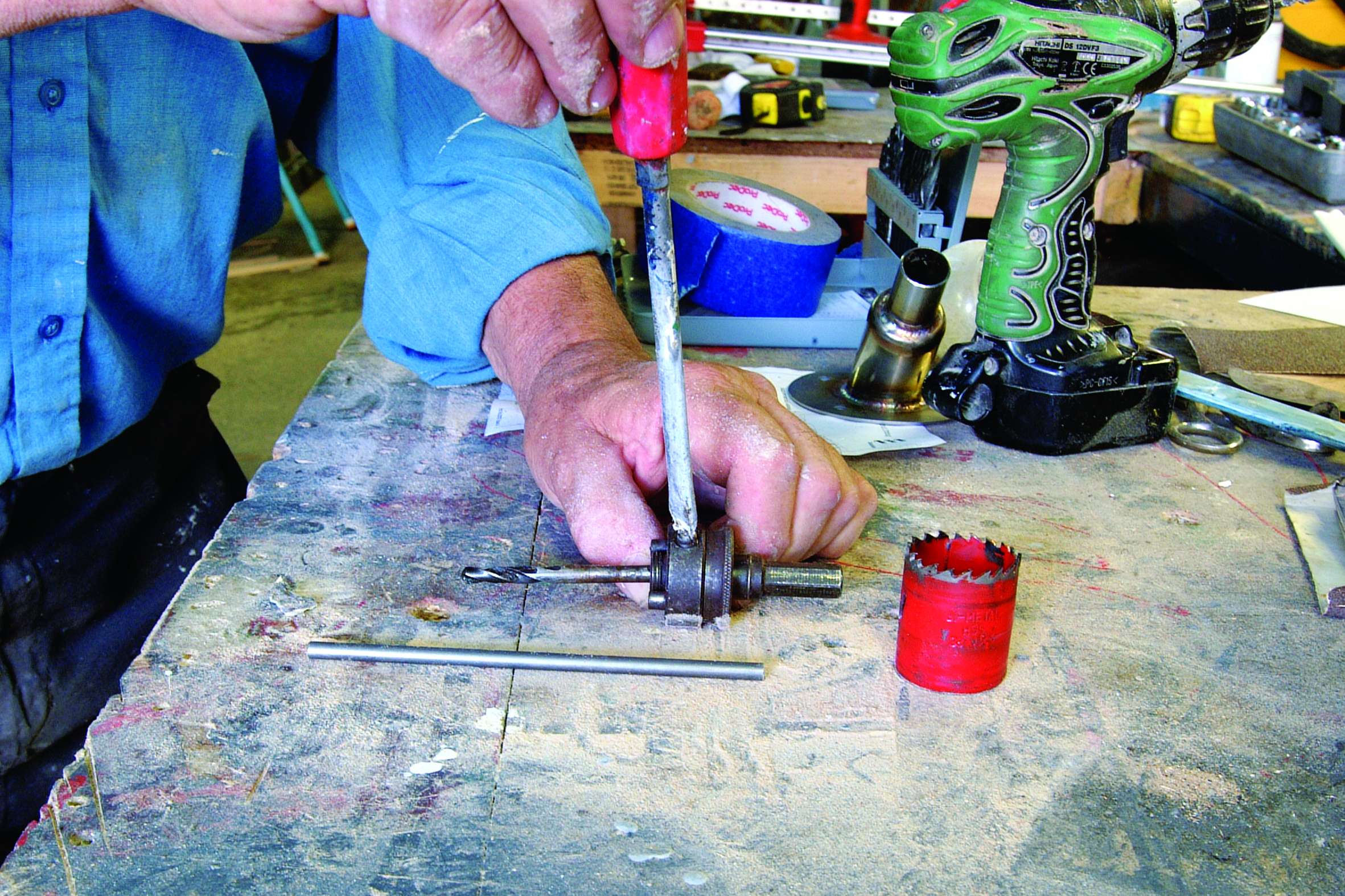 A person uses a hand drill to work on a metal component at a cluttered workbench in what appears to be a boat repair workshop // Photo credit: supplied.