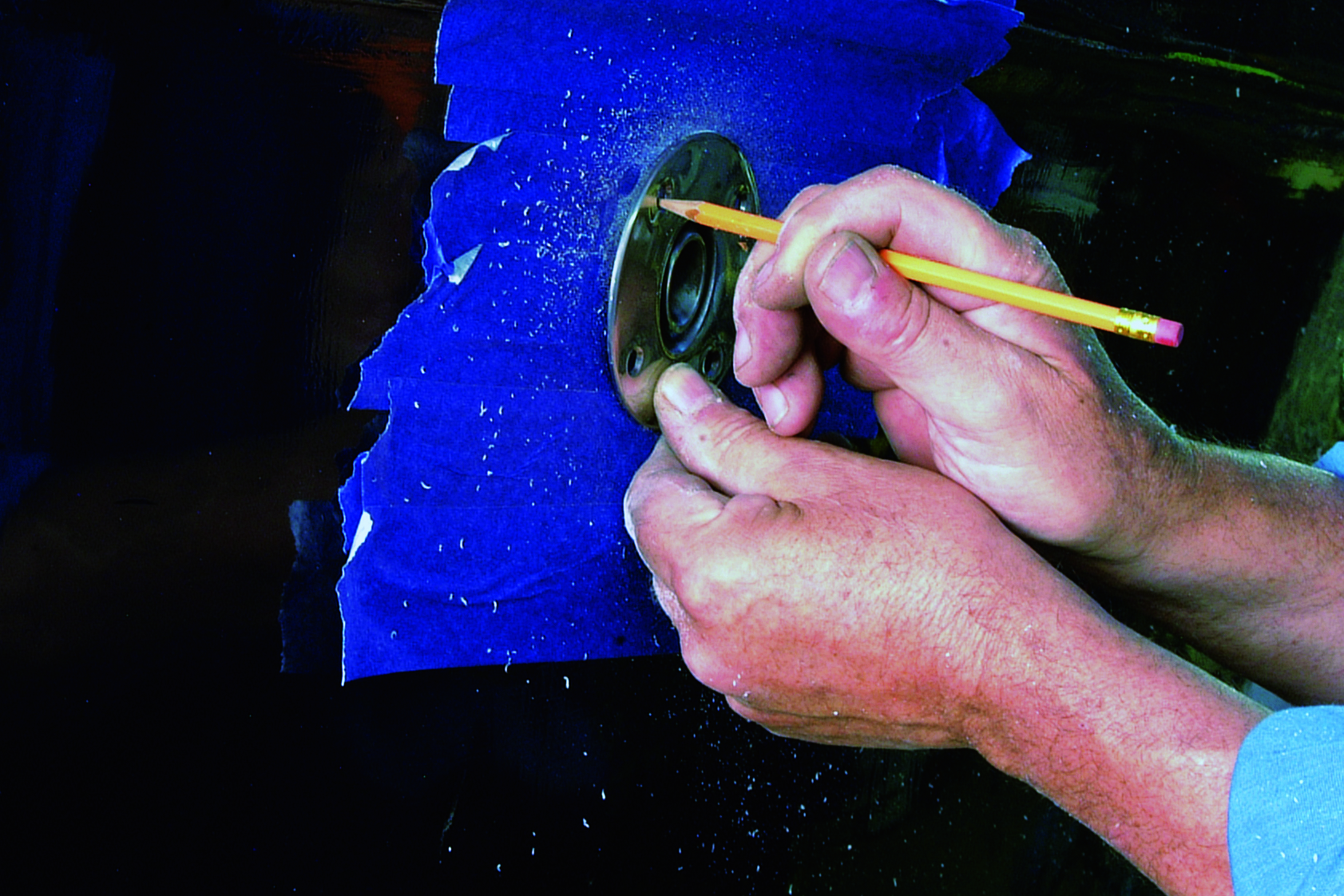 A person uses a pencil to mark measurements on a compass while working on boat maintenance with bright blue antifouling paint visible in the background // Photo credit: supplied.