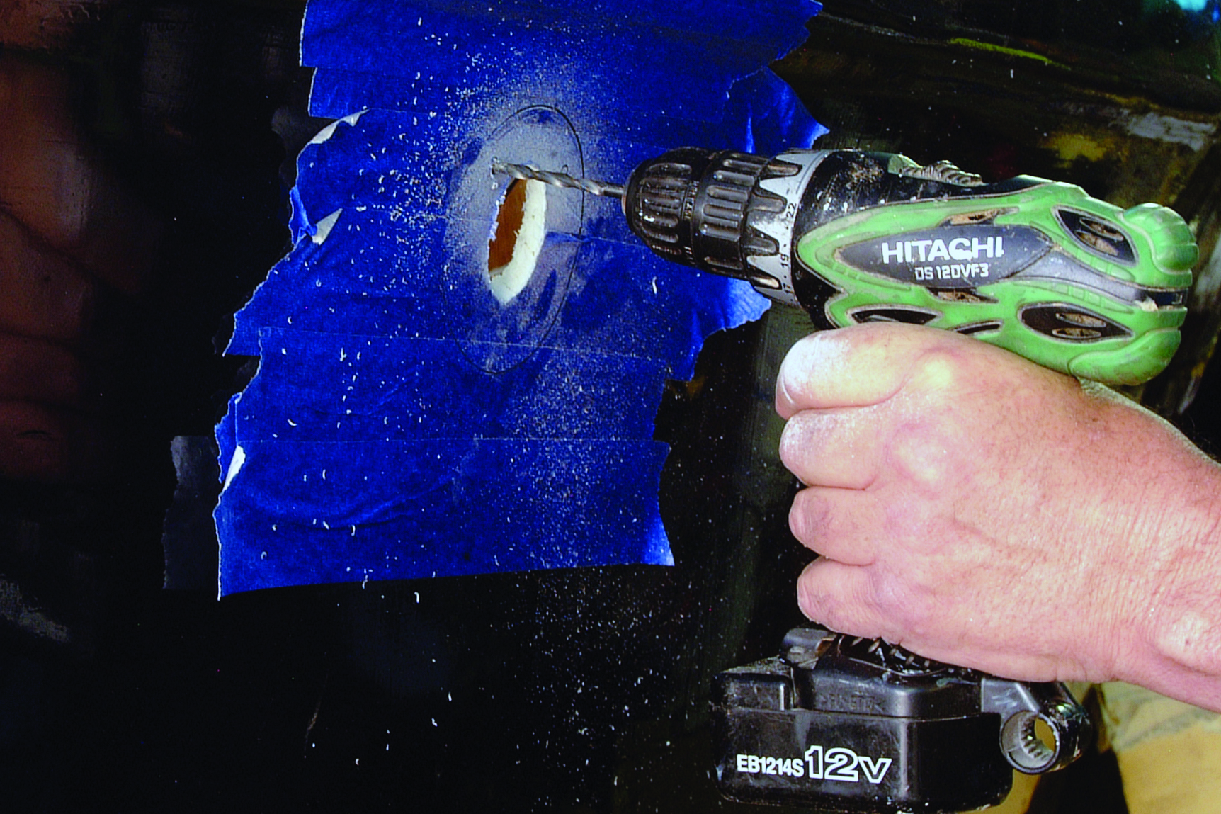 A person uses a Hitachi drill to remove blue antifouling paint from a boat hull during maintenance work // Photo credit: supplied.