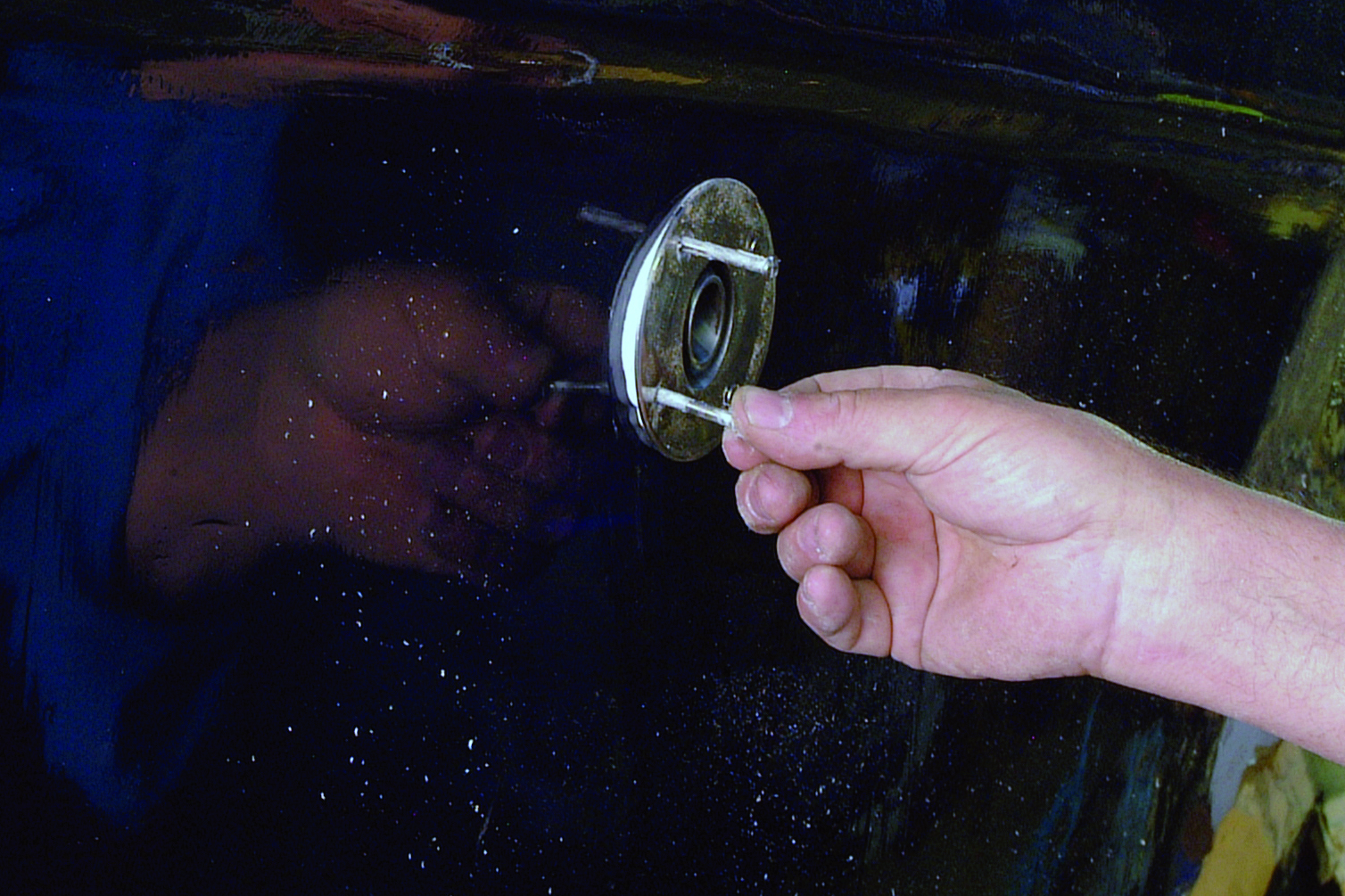 A hand reaches for the chrome door handle of a dark-colored boat amid water droplets on the surface // Photo credit: supplied.