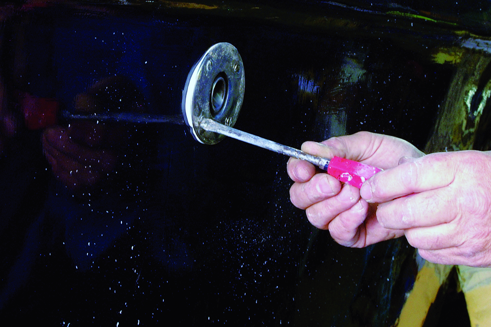 A person holds a large metal spoon or ladle while standing on the wet deck of a boat at night // Photo credit: supplied.
