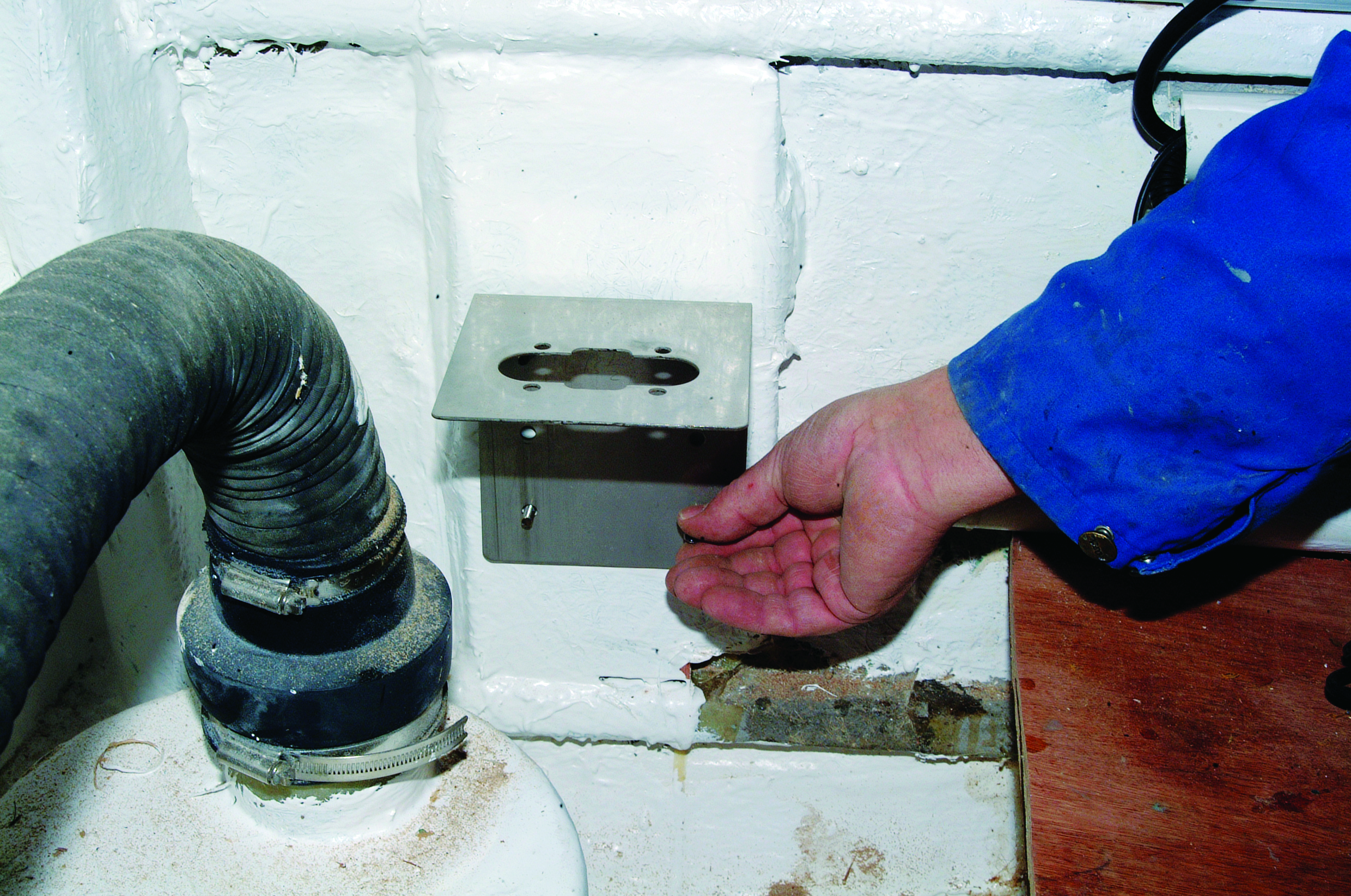 A person in a blue jacket demonstrates the flow from a through-hull fitting in what appears to be a boat's engine compartment or bilge area // Photo credit: supplied.