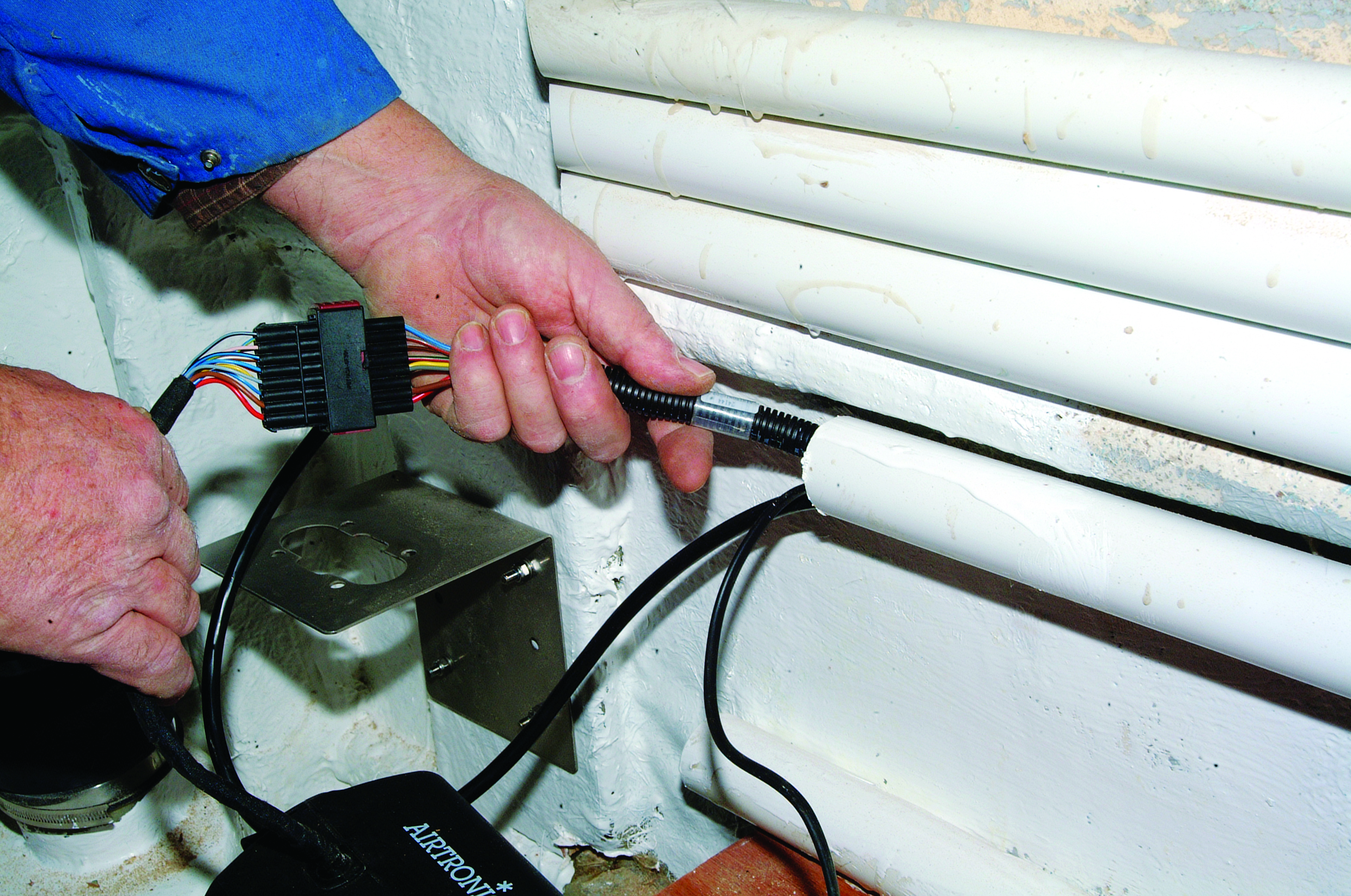 A person installs or connects electrical wiring with a multi-colored connector on a boat named Aircrow // Photo credit: supplied.