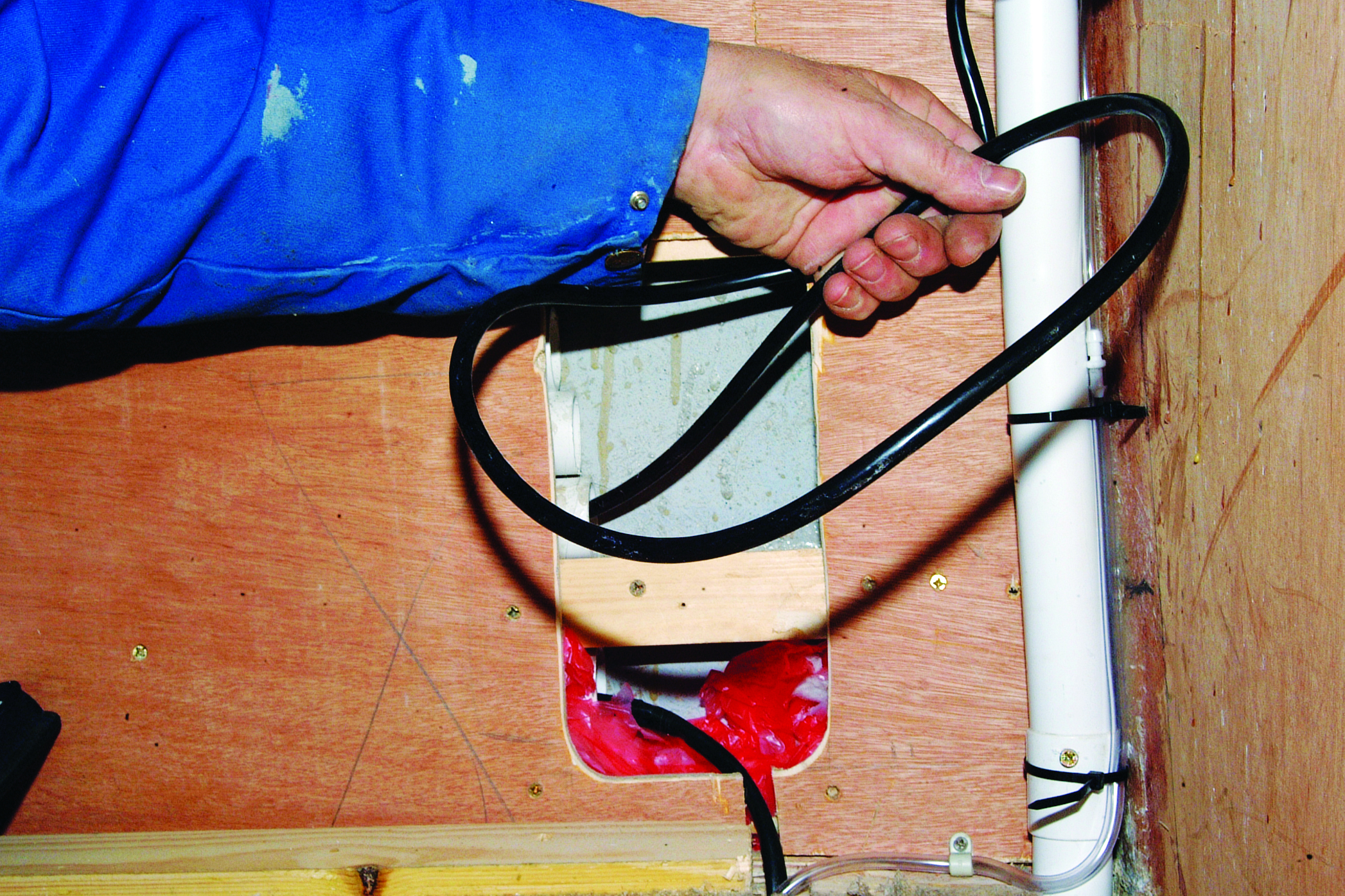 A person in a blue jacket operates a manual bilge pump with red discharge water on a wooden boat deck // Photo credit: supplied.