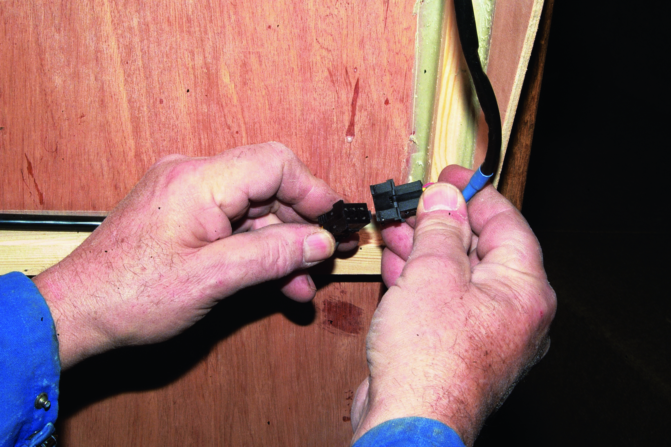 A person's hands work on connecting or adjusting black electrical components on wooden boat hardware // Photo credit: supplied.