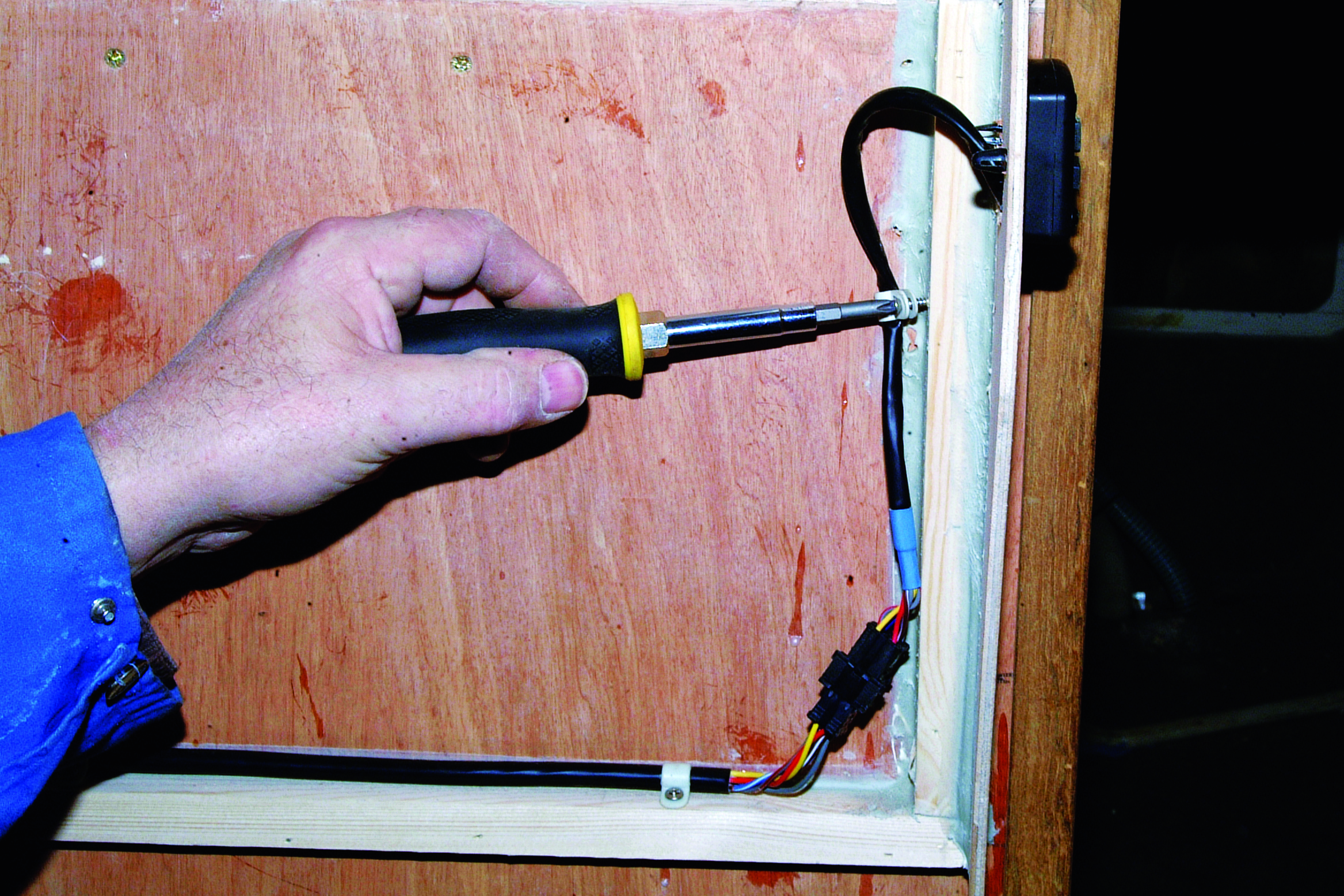 A person uses a soldering iron to work on electrical wiring connections inside what appears to be a boat's interior compartment // Photo credit: supplied.
