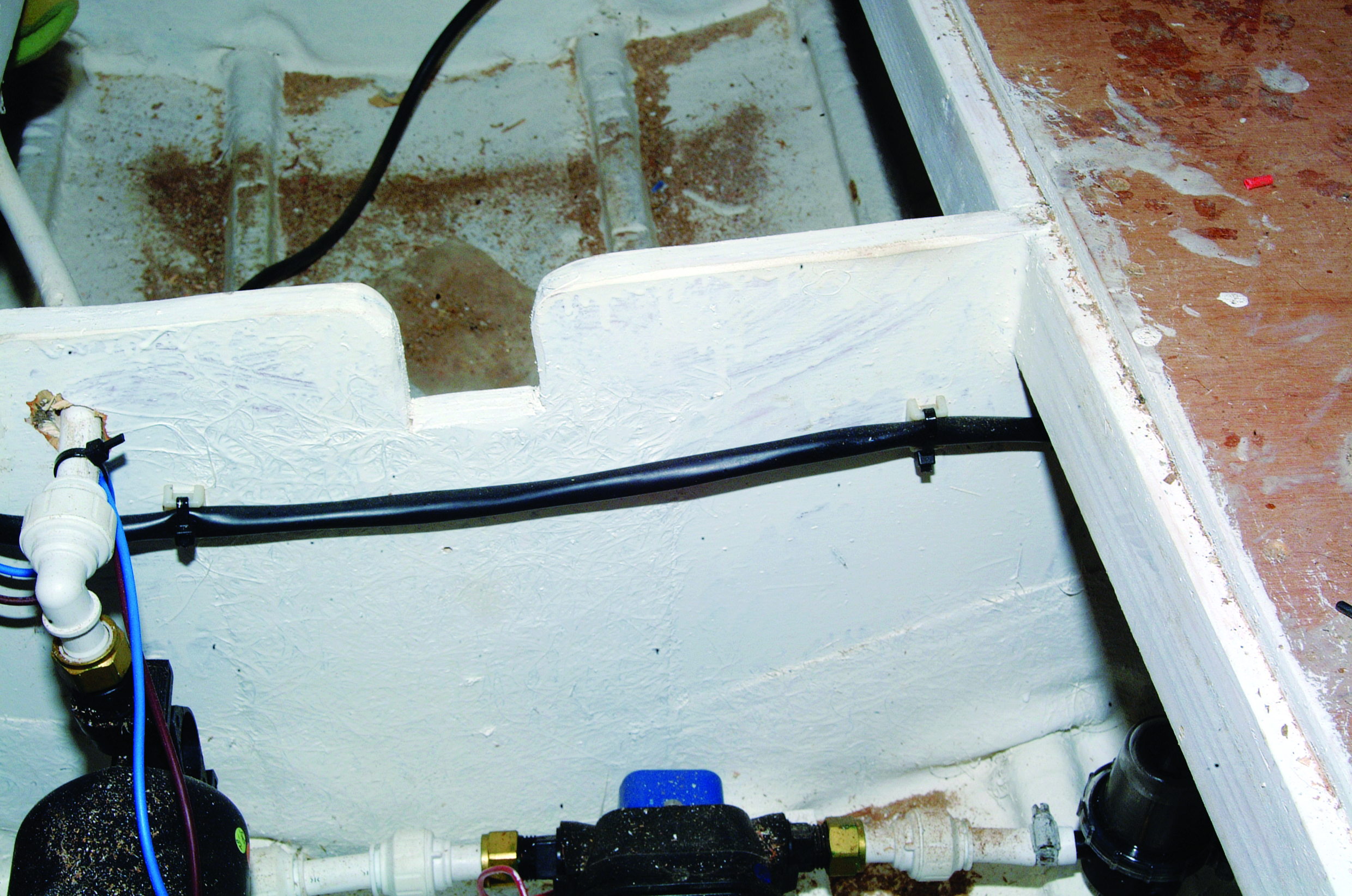 A close-up view of a boat's bilge area showing water pumping equipment with hoses and fittings installed in the white fiberglass hull // Photo credit: supplied.