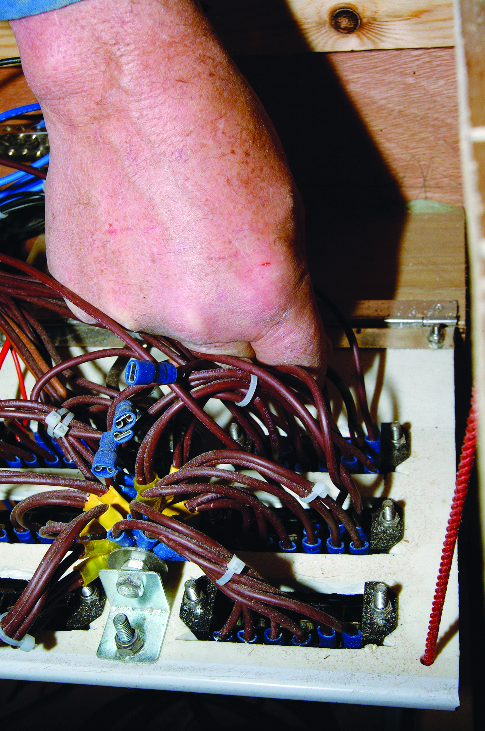 A person's sunburned leg is visible above an electrical panel with multiple brown wires and blue connectors on what appears to be a boat // Photo credit: supplied.