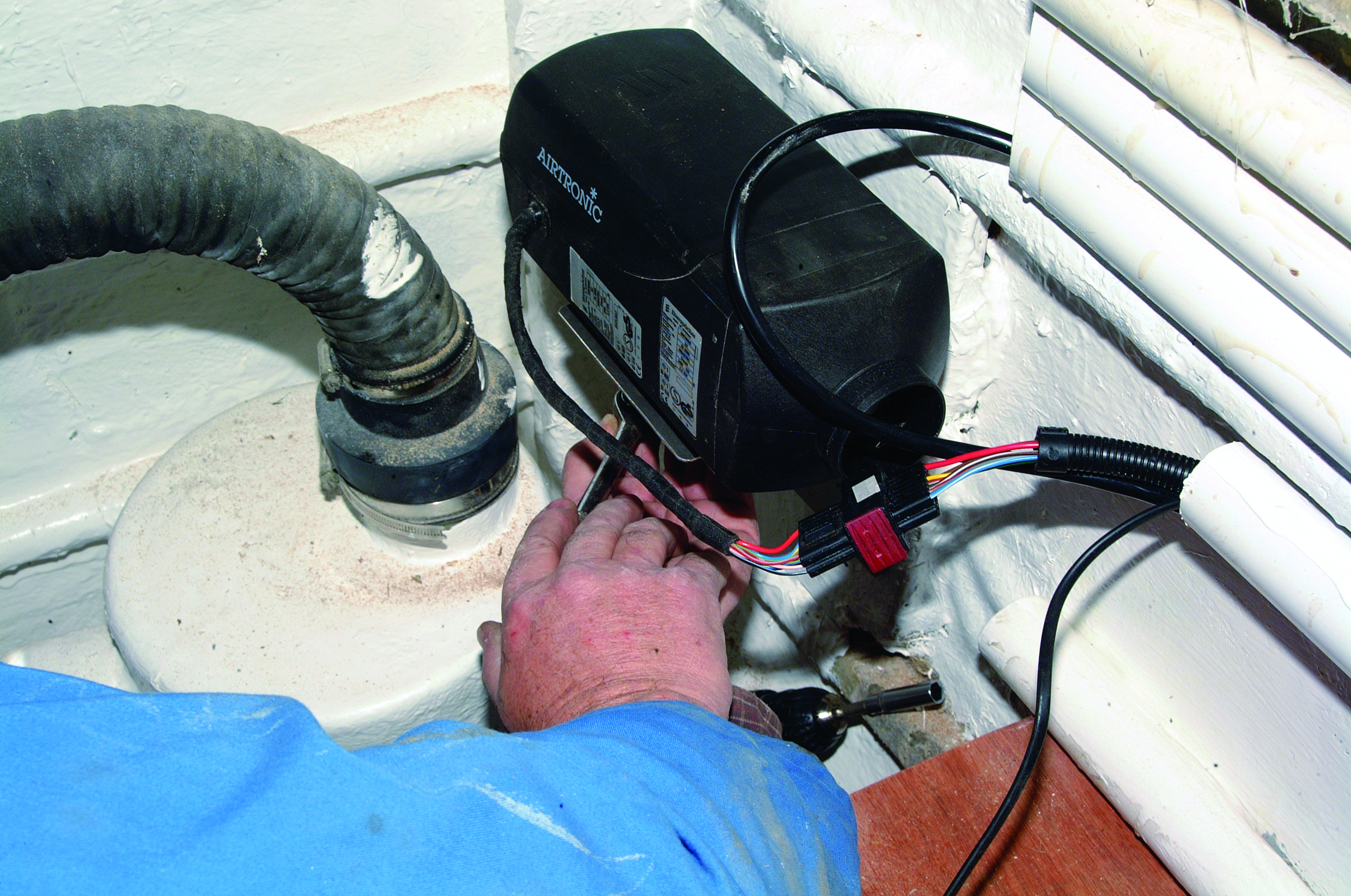 A person works on installing or repairing electrical wiring connected to a black marine device in a boat's engine compartment or bilge area // Photo credit: supplied.