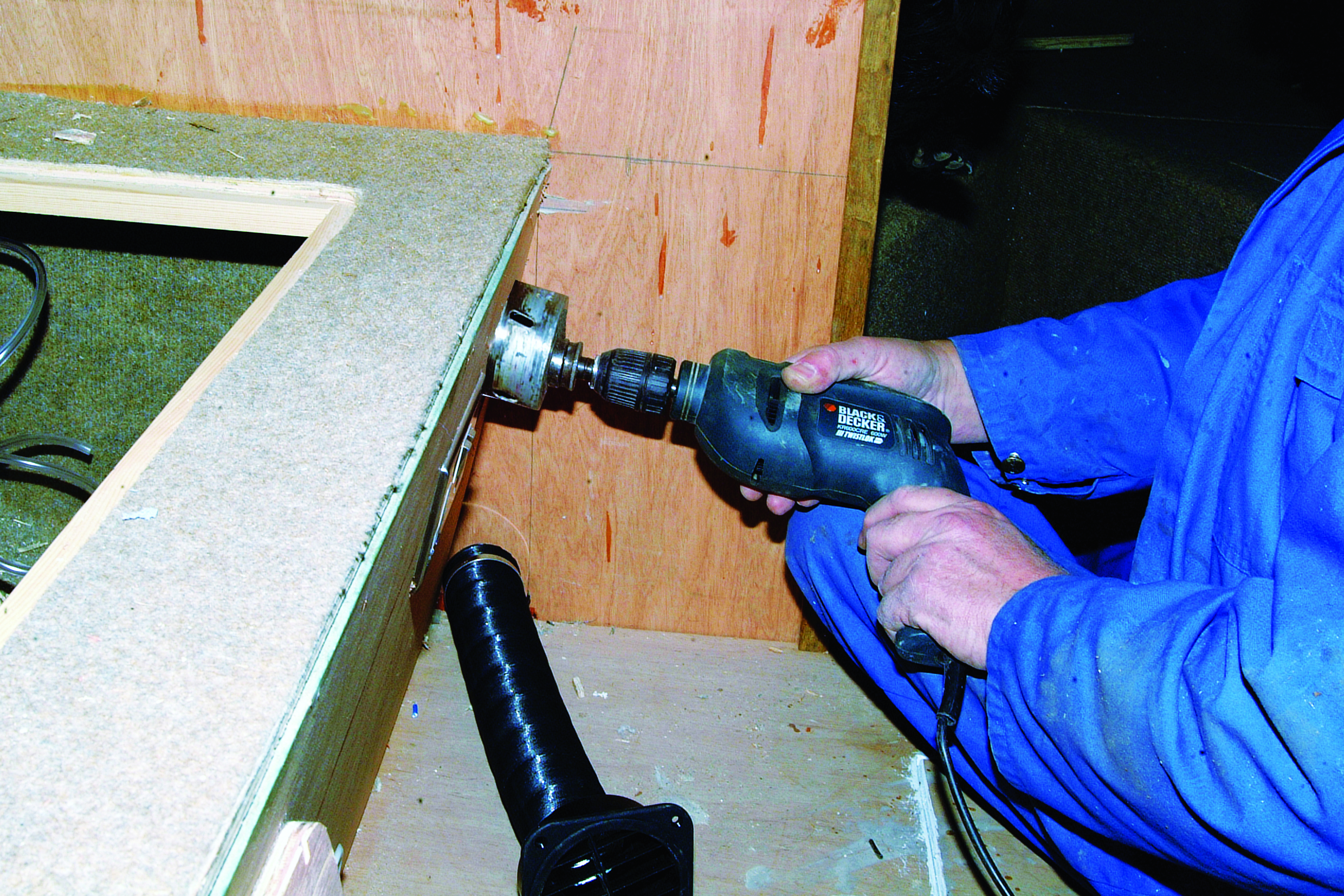 A person in blue clothing uses a Black & Decker drill to work on wooden cabinetry inside a boat's interior // Photo credit: supplied.