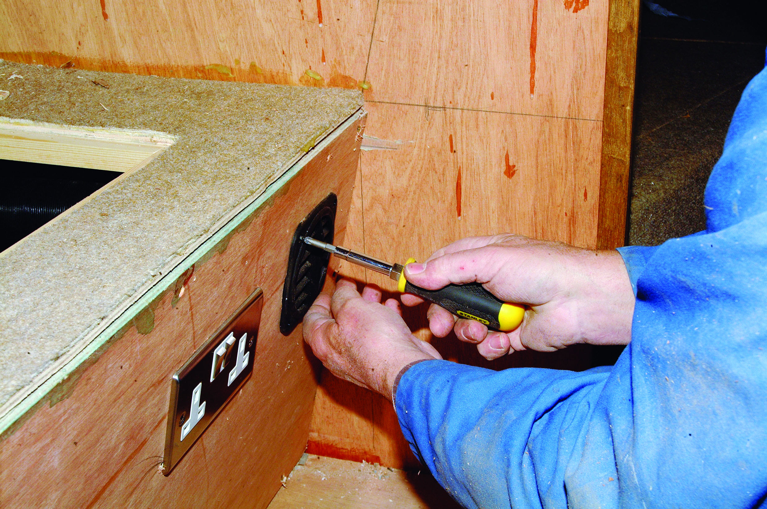 A person uses a screwdriver to install hardware on the wooden interior of a boat under construction // Photo credit: supplied.