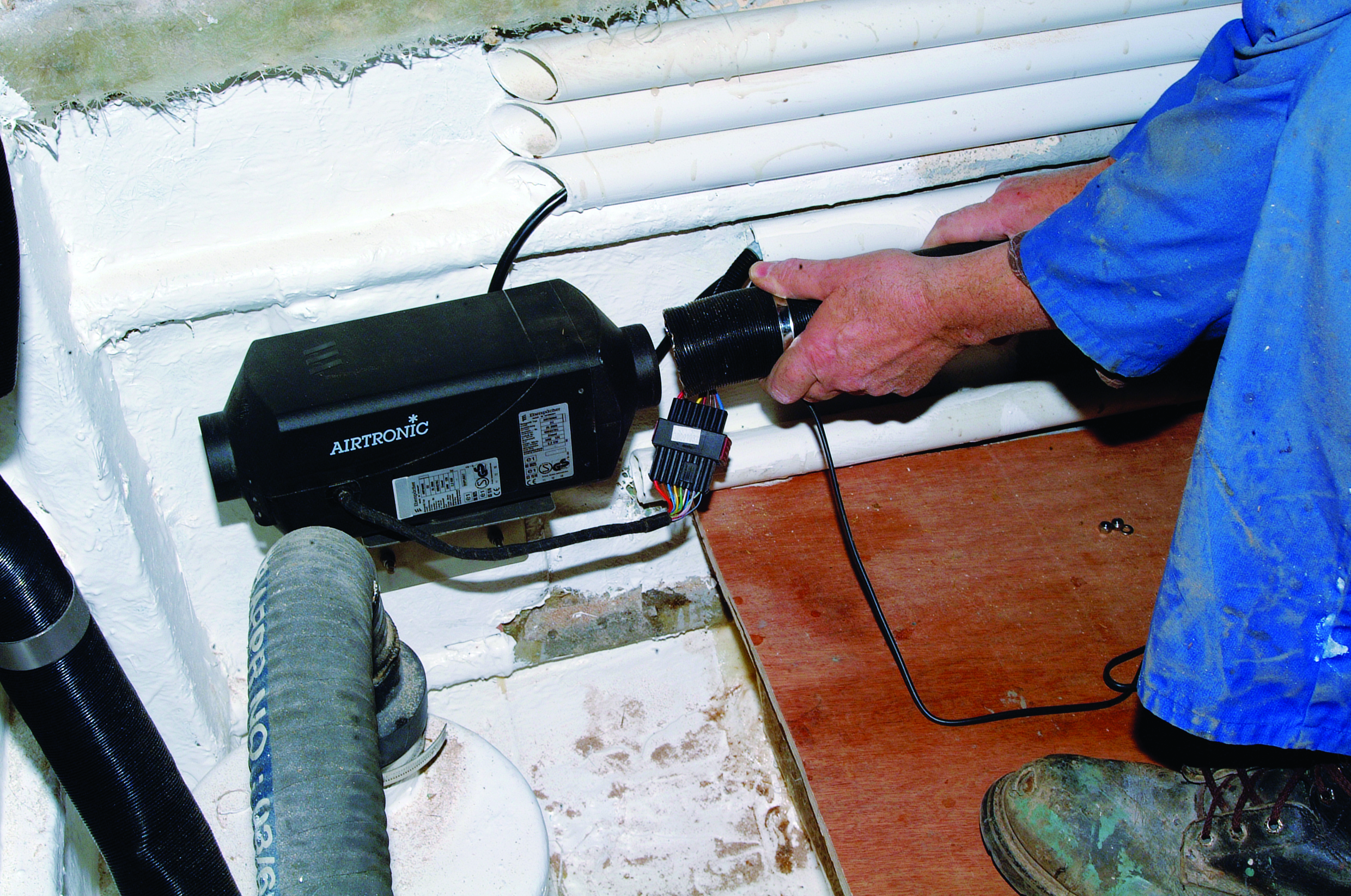 A person installs an Airtronic heating unit in the engine compartment of a sailboat // Photo credit: supplied.