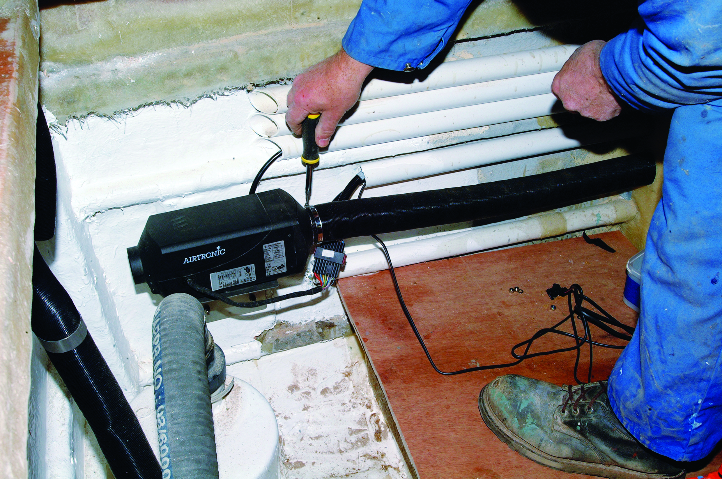 A person in blue clothing operates an Airtronic heating unit while working on boat maintenance in what appears to be a vessel's interior compartment // Photo credit: supplied.
