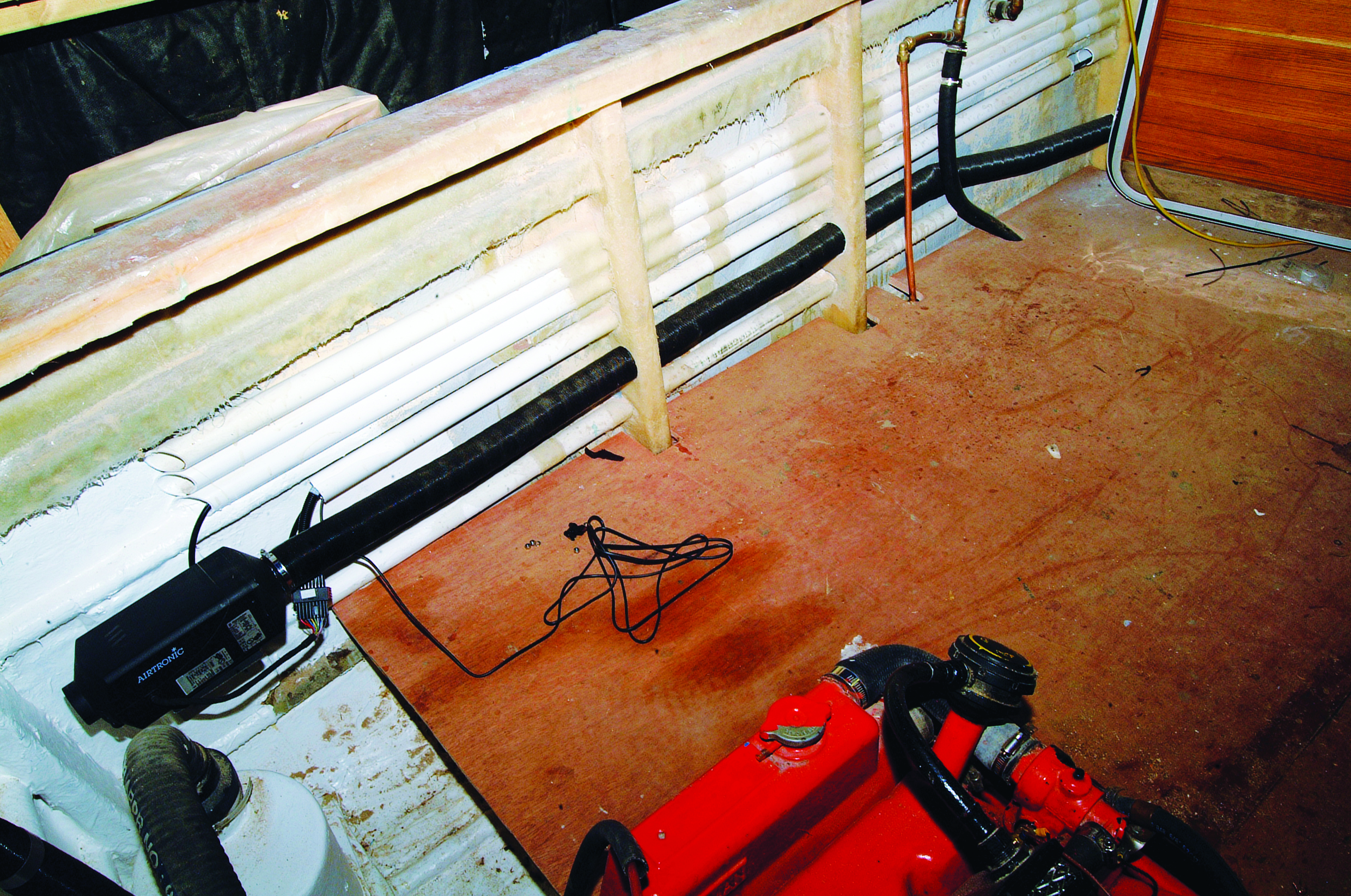 A boat deck shows diving equipment including red scuba tanks and black gear laid out on the wooden surface, with white railings and calm water visible alongside // Photo credit: supplied.