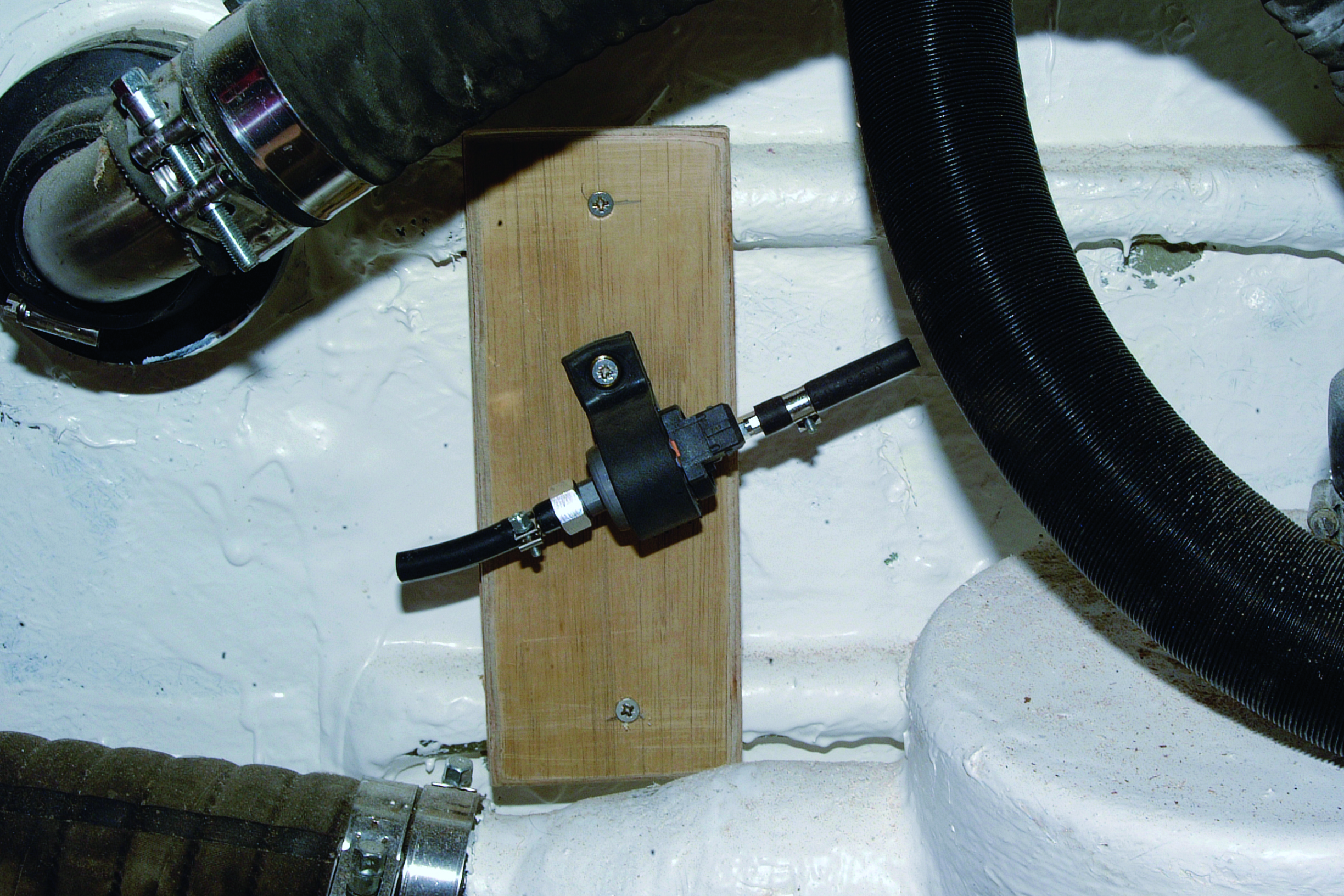 A wooden mounting block with a black fitting is installed in the white fiberglass hull of a boat, surrounded by hoses and mechanical components // Photo credit: supplied.