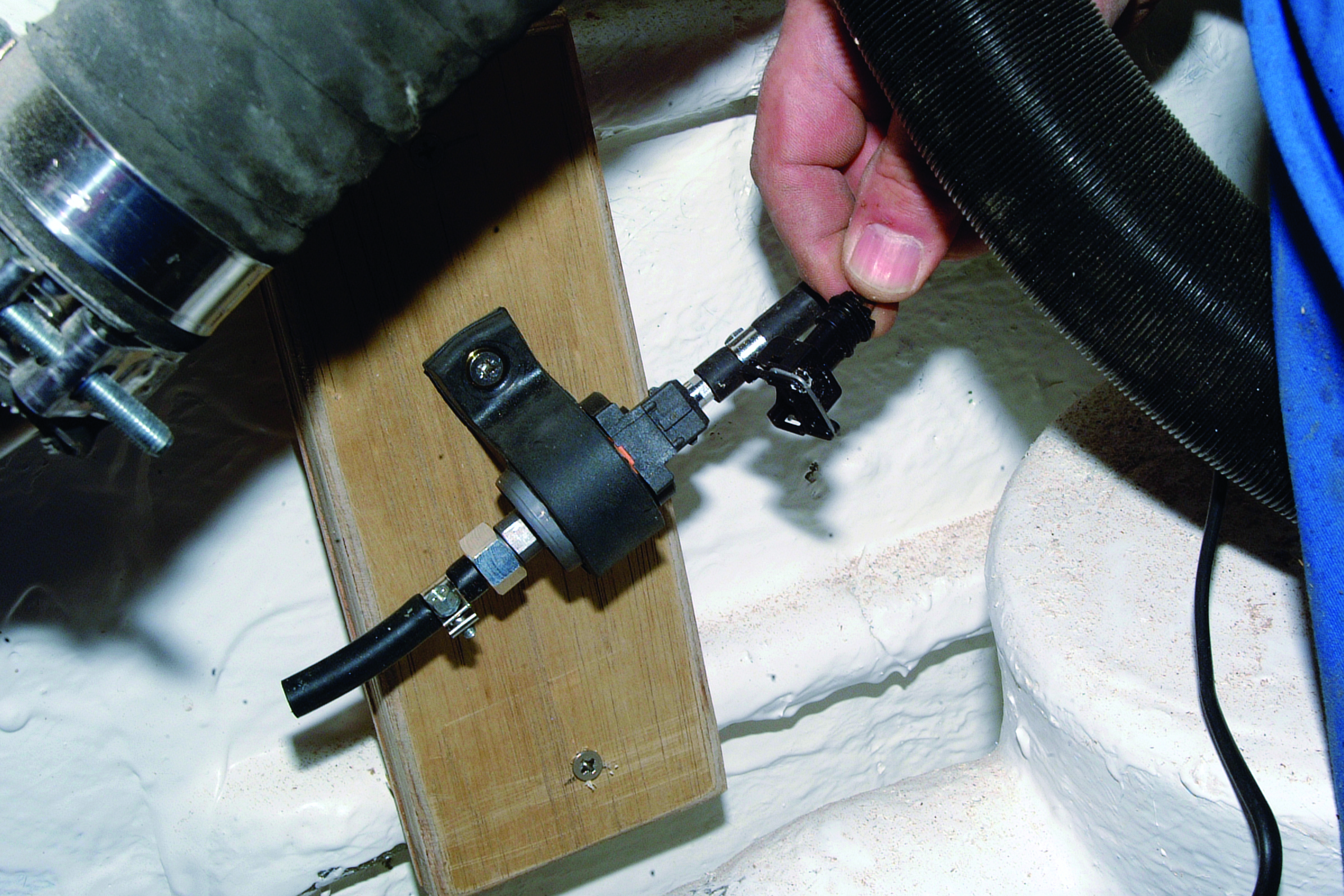 A person's hand adjusts a black fuel injector or engine component mounted on a wooden block inside a boat's engine compartment // Photo credit: supplied.