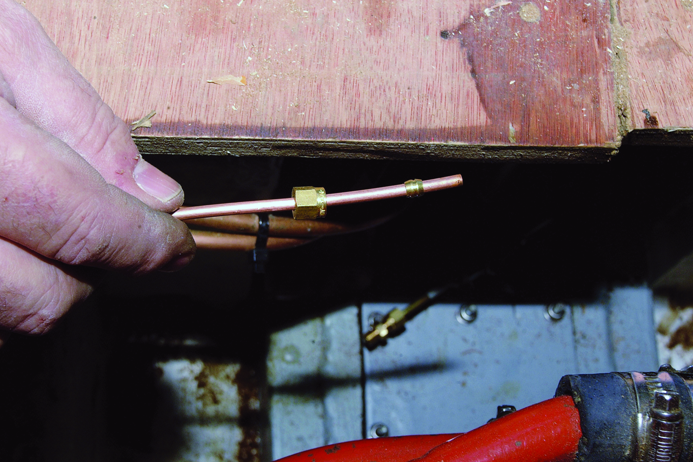 A hand holds a copper fuel line with brass fitting during boat engine maintenance or repair work // Photo credit: supplied.
