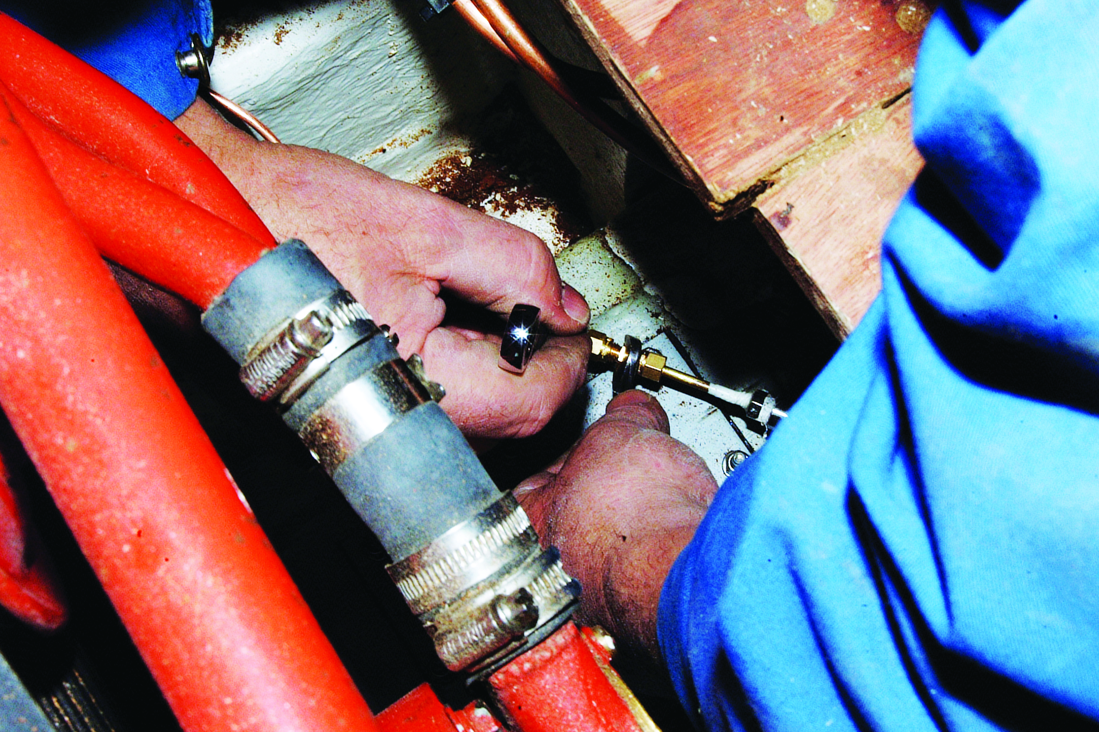 A person's hands work on connecting or adjusting metal fittings and hoses on what appears to be boat equipment or rigging // Photo credit: supplied.