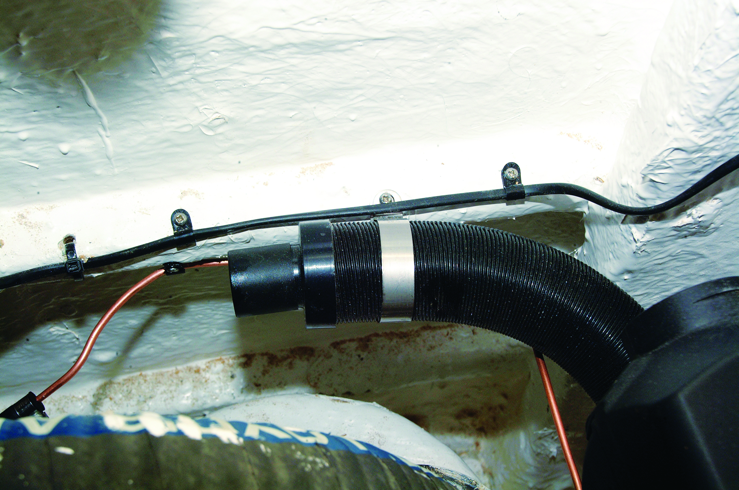 A marine bilge pump system with black corrugated hose and red wiring is installed in the hull of a boat floating on water // Photo credit: supplied.
