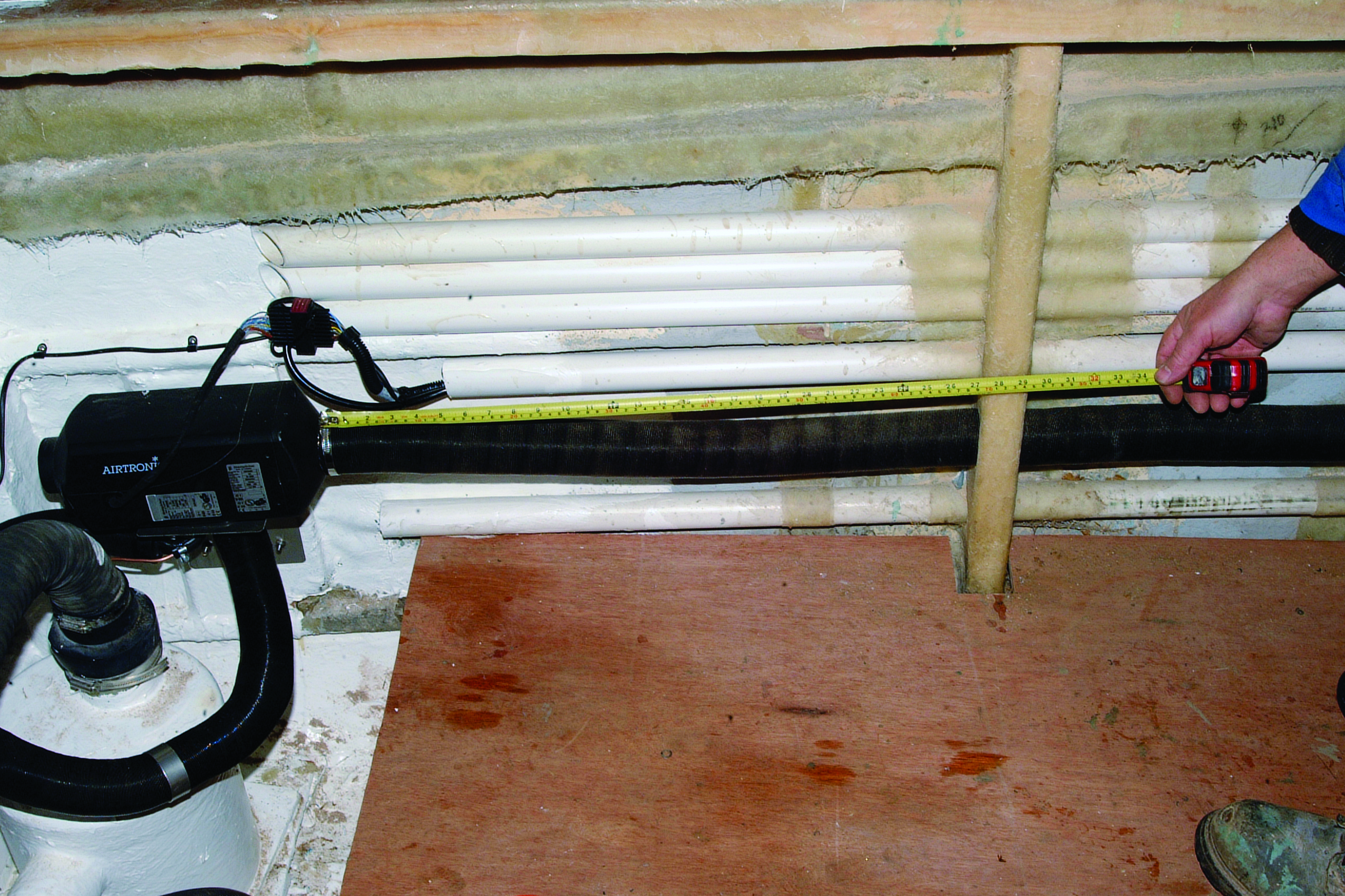 A person measures the hull of a white boat using a measuring tape while a shop vacuum sits nearby during what appears to be maintenance or repair work // Photo credit: supplied.