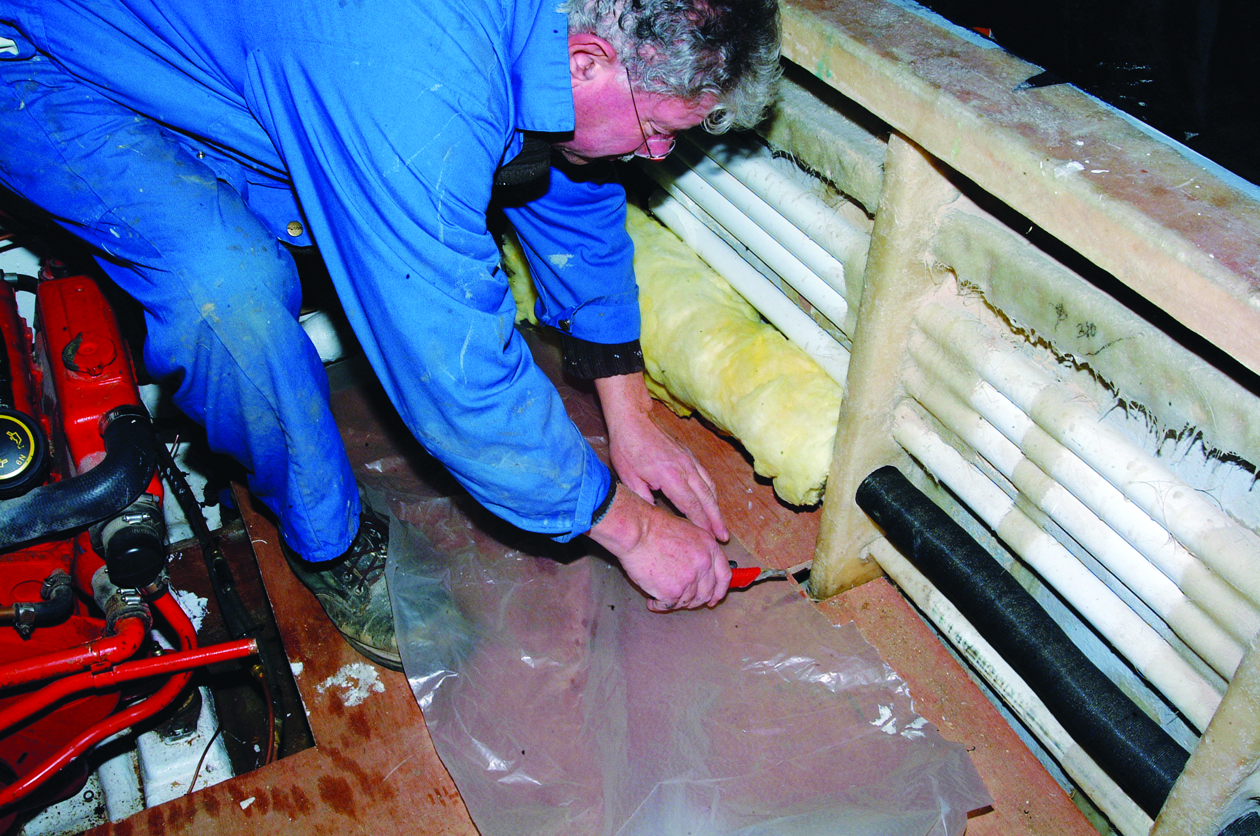 A person in blue coveralls works on maintenance or repairs in the bilge area of a boat's engine compartment // Photo credit: supplied.