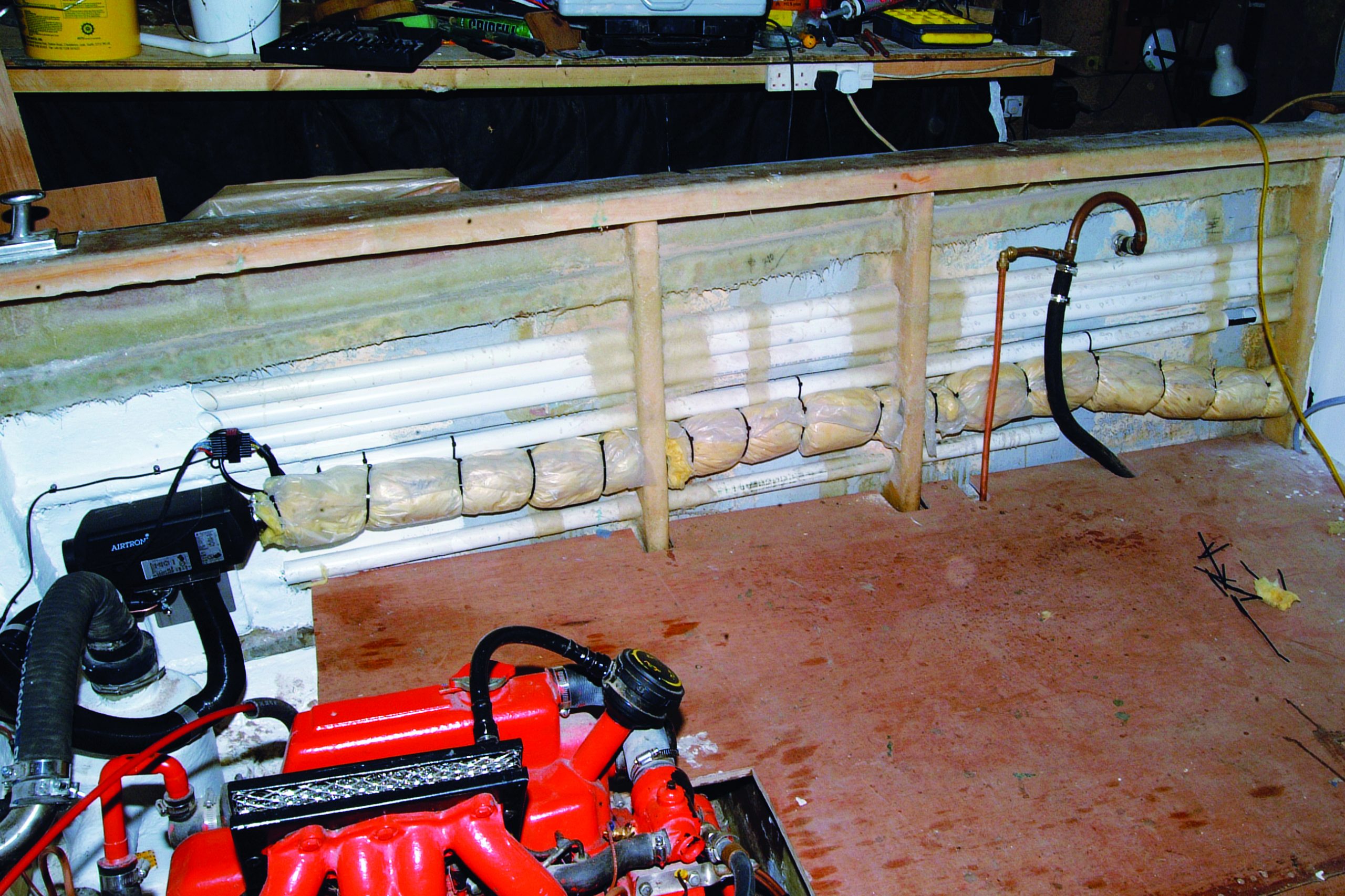 A boat's engine compartment and hull interior during restoration work, showing the red engine block alongside exposed wooden ribs and insulation materials in what appears to be a workshop setting // Photo credit: supplied.