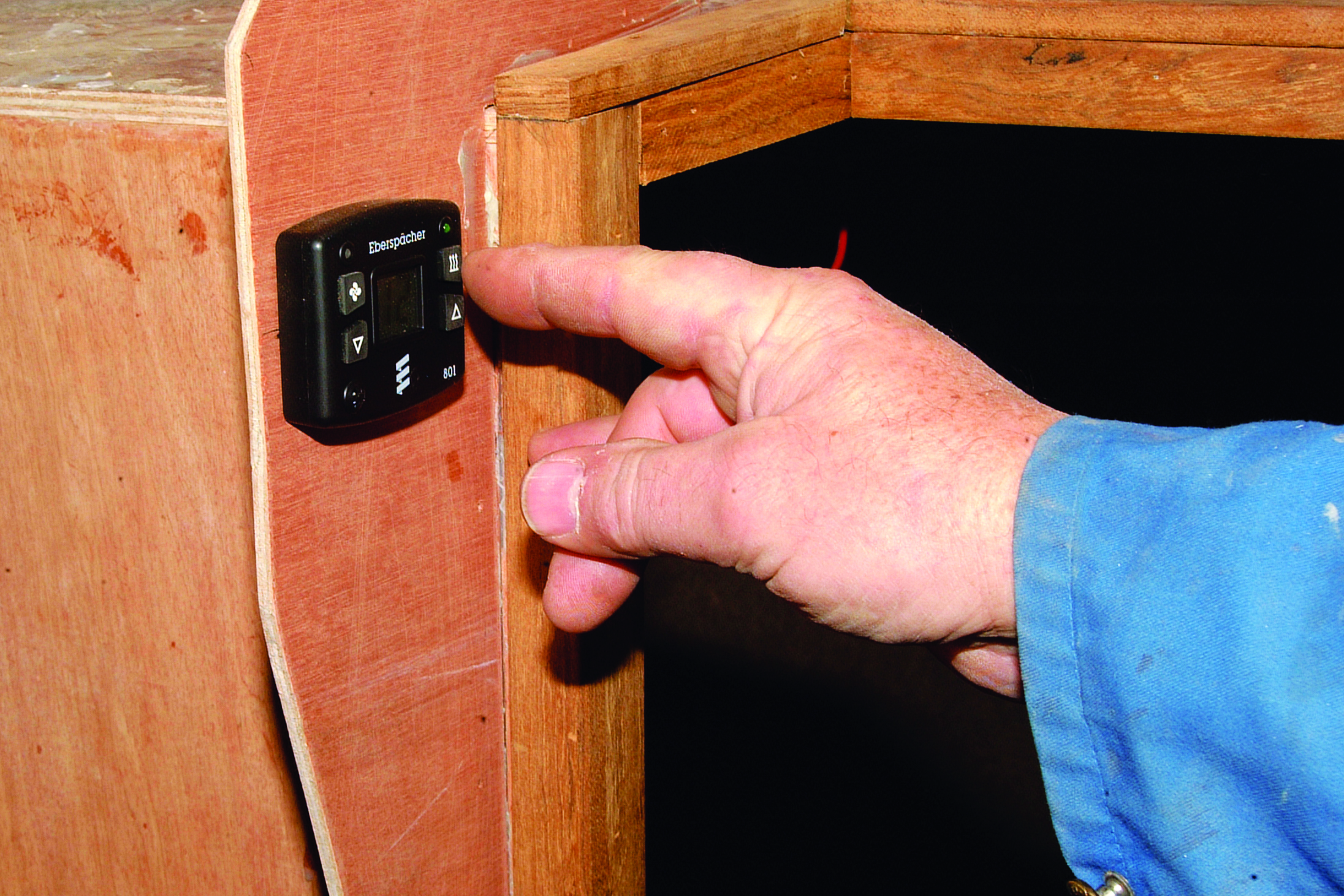 A person operates a black electronic control device mounted on the wooden interior of a boat // Photo credit: supplied.