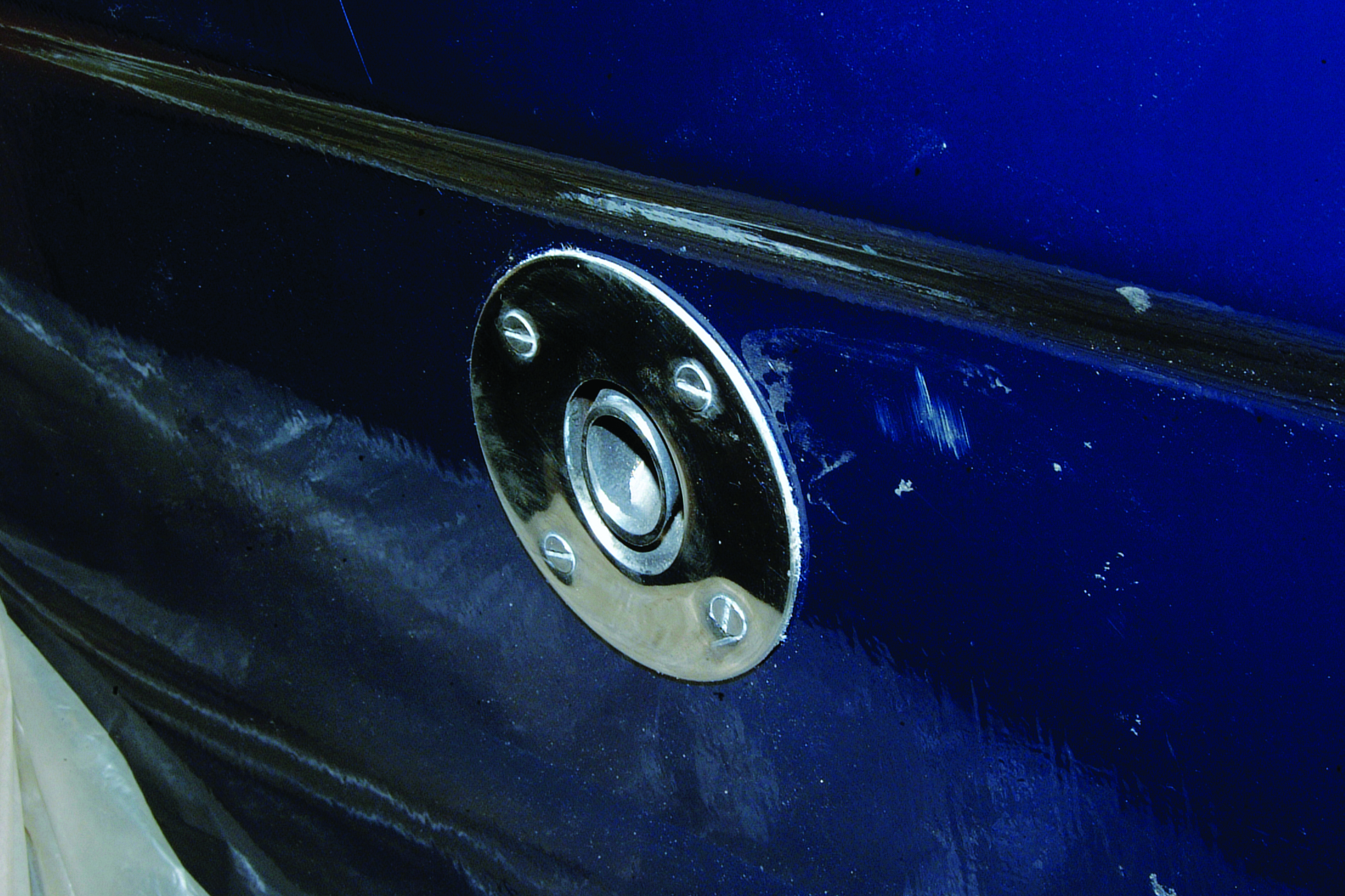 A circular metal fitting with a central button is mounted on the blue hull of a boat // Photo credit: supplied.