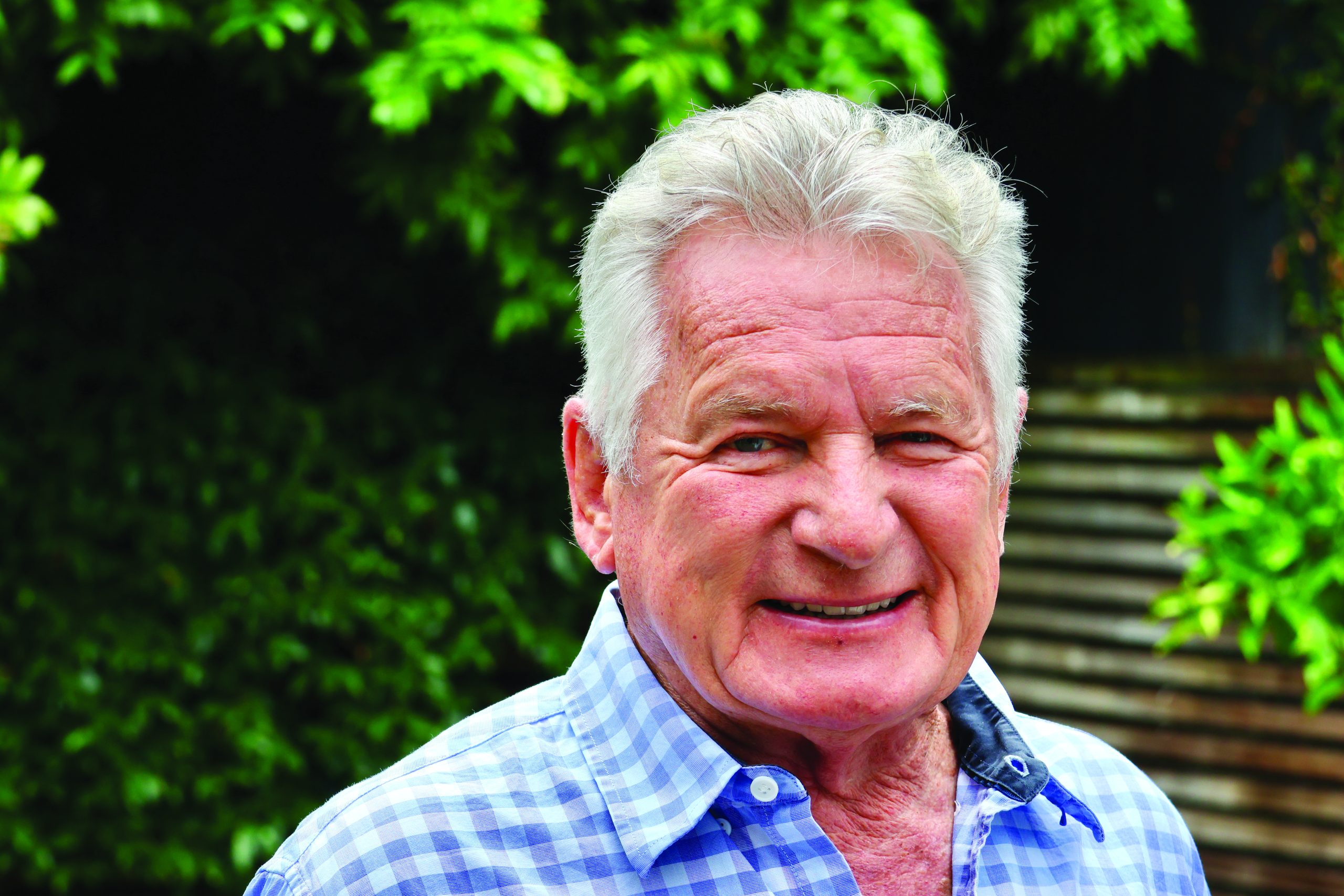 I don't see any boating content in this image. The image shows an older man with silver/white hair wearing a blue and white checkered shirt, standing outdoors with green foliage in the background. There are no boats, vessels, water, or marine-related elements visible in this photograph // Photo credit: supplied.
