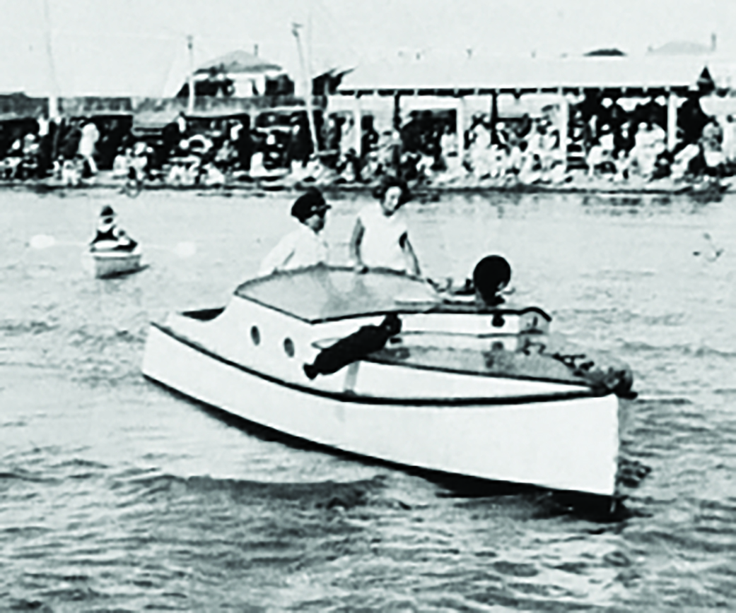 A small white motorboat with passengers cruises through choppy waters near a crowded waterfront with spectators gathered along the shore // Photo credit: supplied.