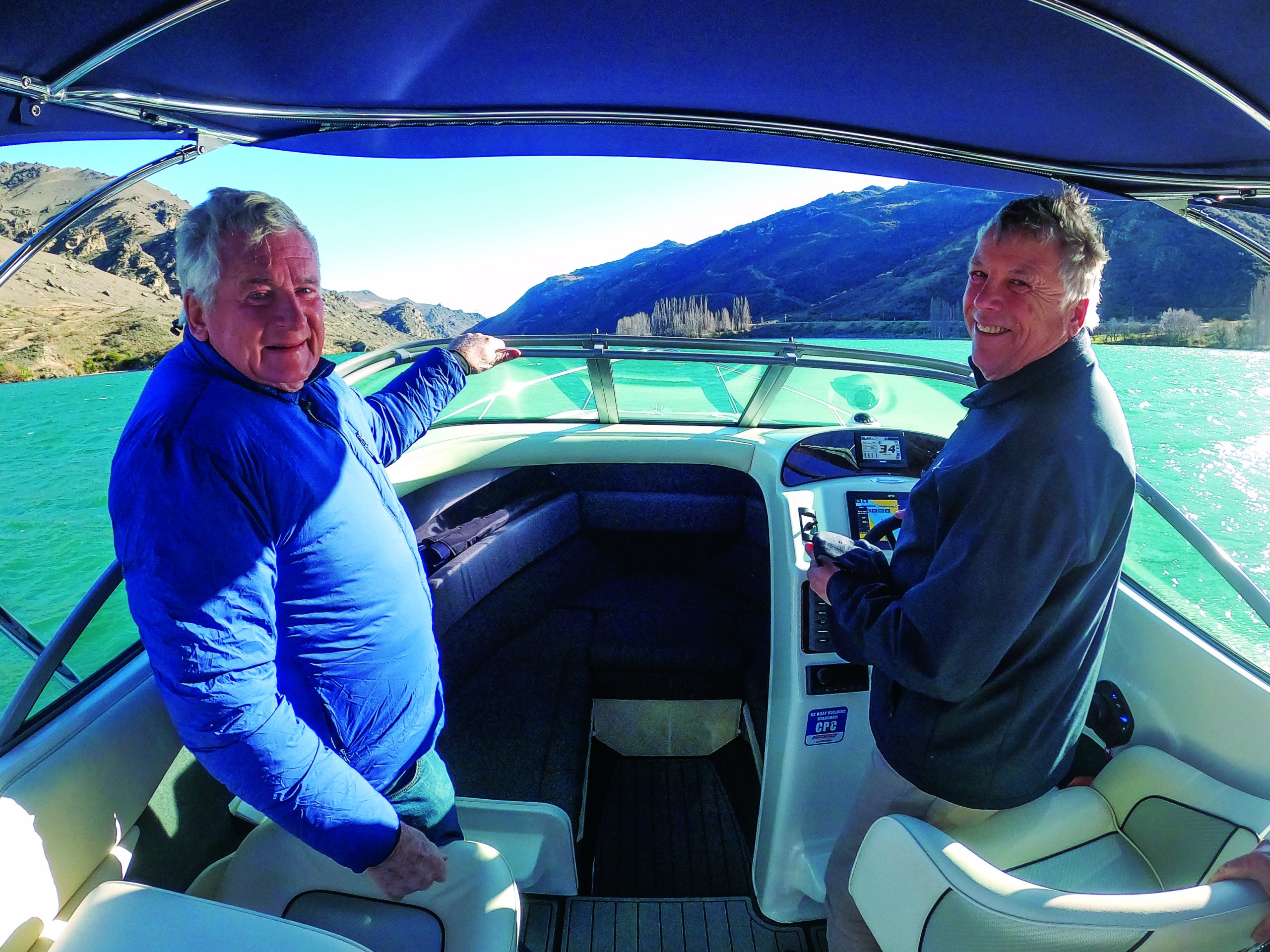 Two men enjoy a sunny day boating on turquoise waters surrounded by dramatic mountains and hills // Photo credit: supplied.