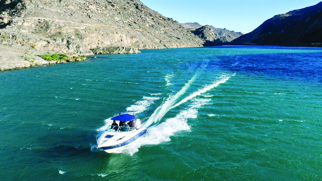 A speedboat creates a dramatic wake while cruising across the turquoise waters of a mountain-surrounded lake // Photo credit: supplied.