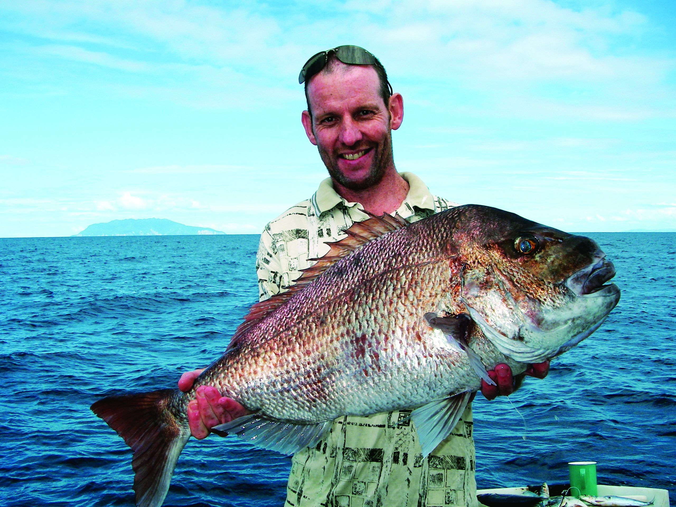 A smiling angler displays a large snapper while fishing on open blue waters // Photo credit: supplied.