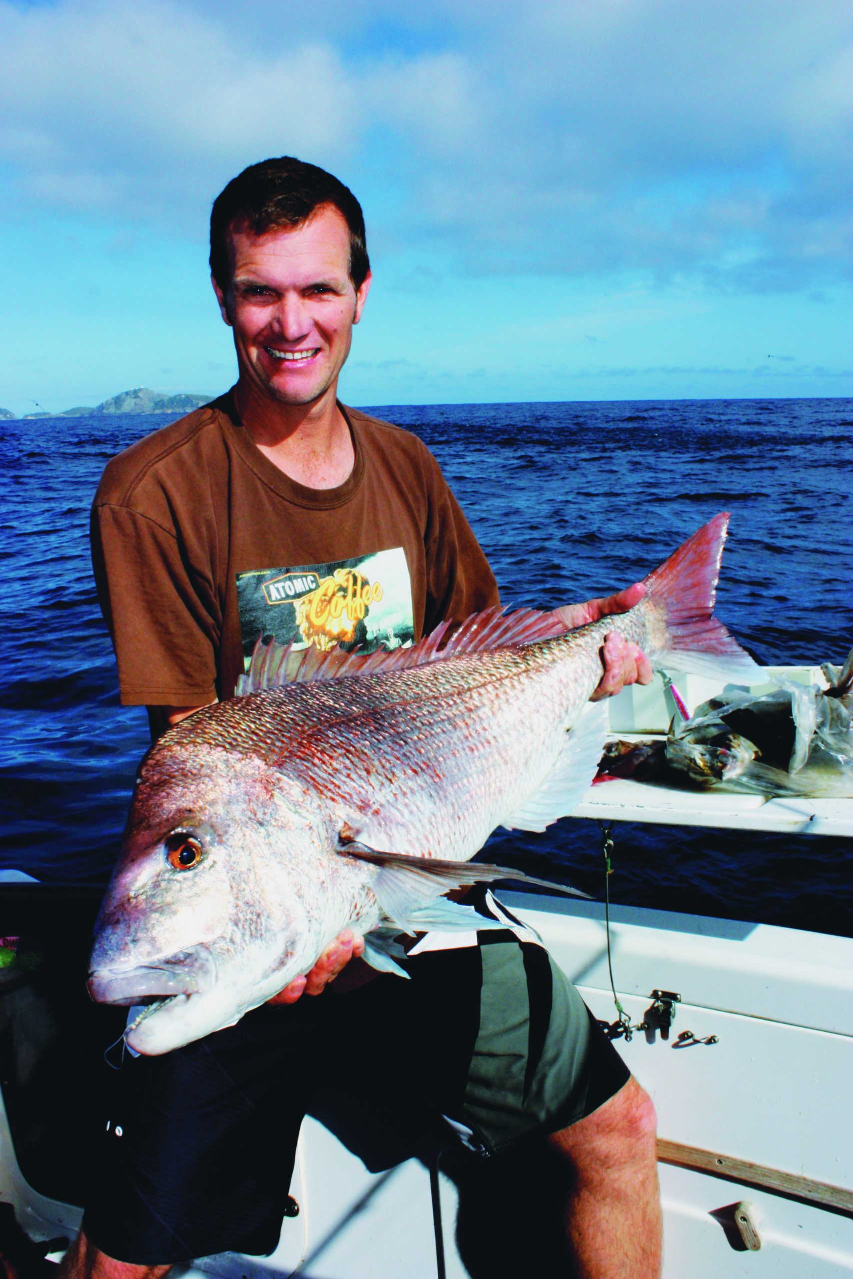 A smiling angler displays his large catch while seated on a fishing boat in open blue waters // Photo credit: supplied.